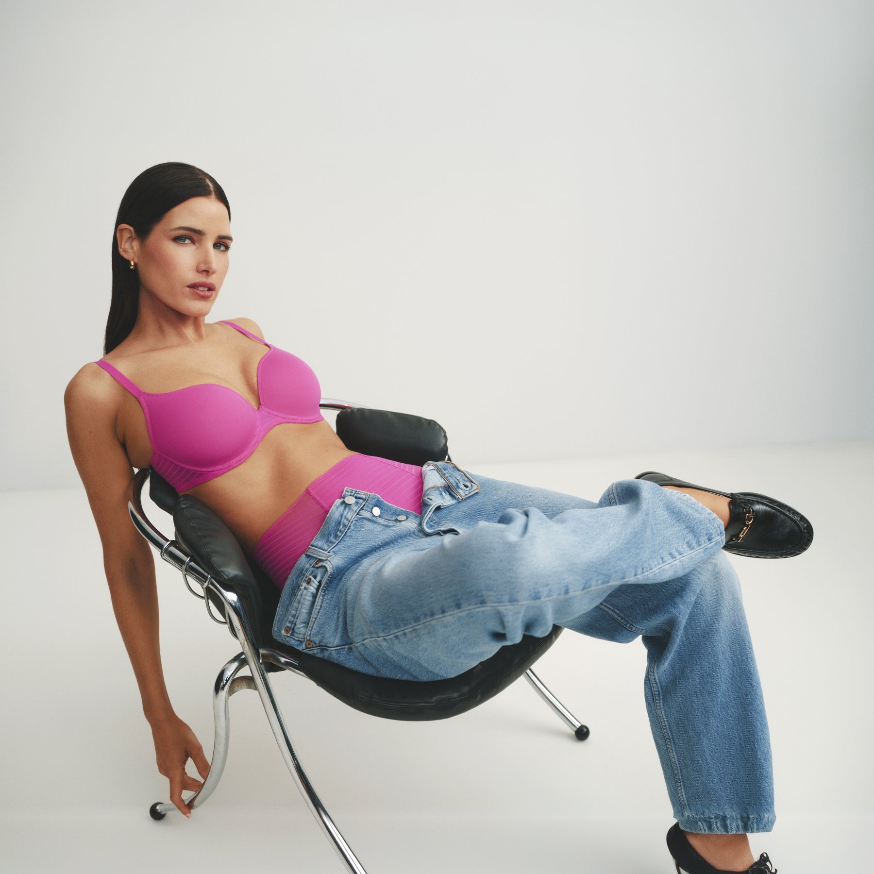 Model lounging in a chair wearing the very berry pink seamless T-shirt bra with matching high-waist briefs, styled with relaxed blue jeans for a modern everyday look.
