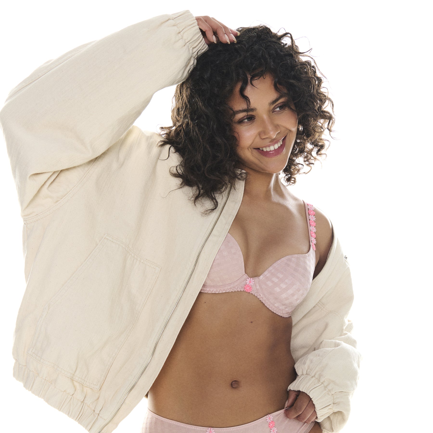 Model smiling in pastel pink gingham lingerie set under an oversized cream jacket.