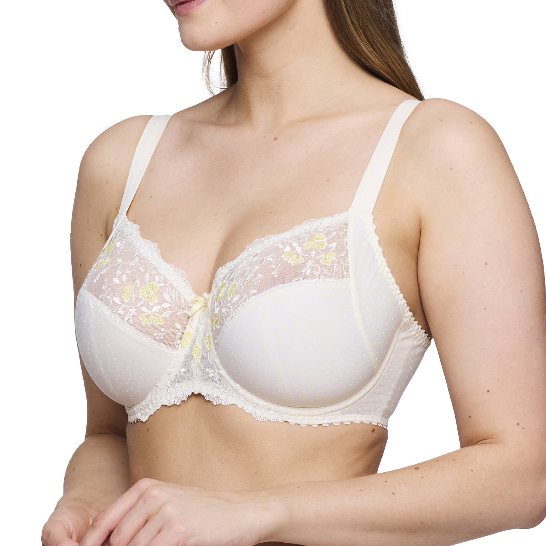 Angled front view of a woman wearing a cream embroidered bra with light yellow floral lace and dot details.