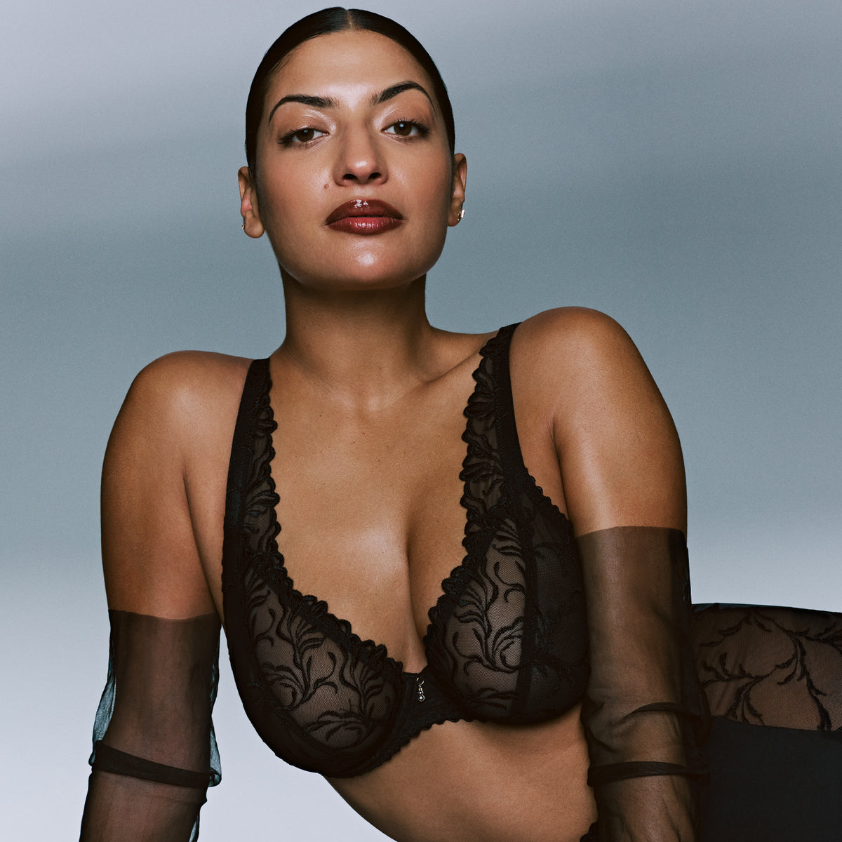 Model wearing the PrimaDonna Solisse Plunge Bra in black, featuring sheer floral embroidery and a flattering deep neckline.