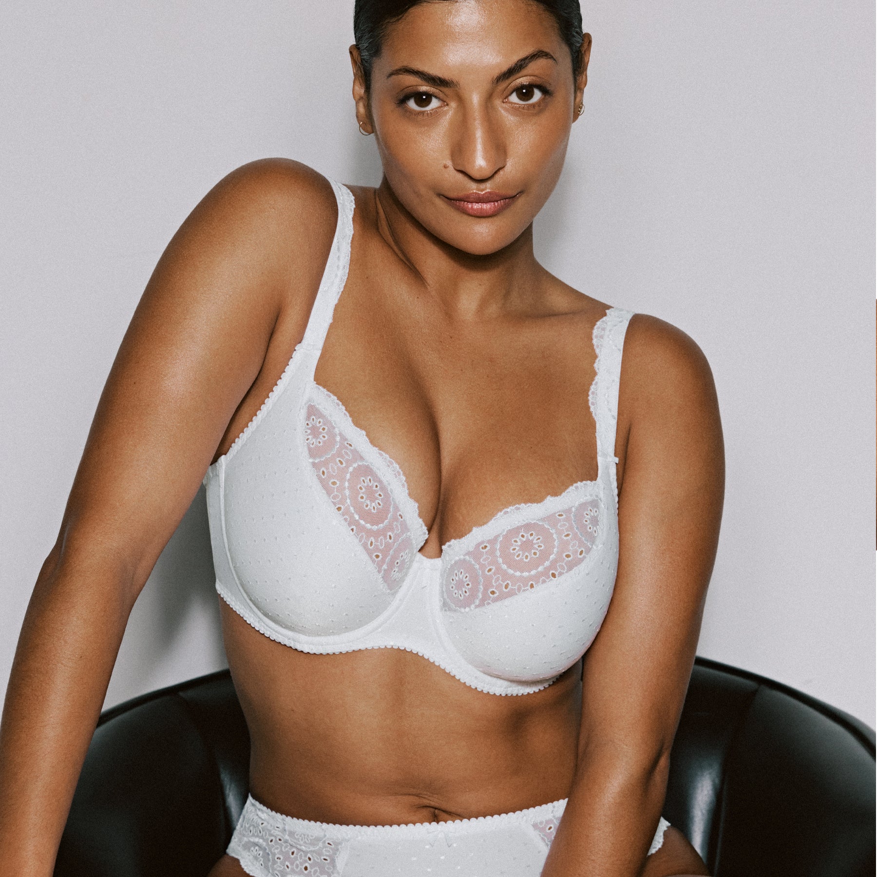 Model wearing white lace and embroidered underwire bra with dotted fabric cups and sheer lace upper panels.