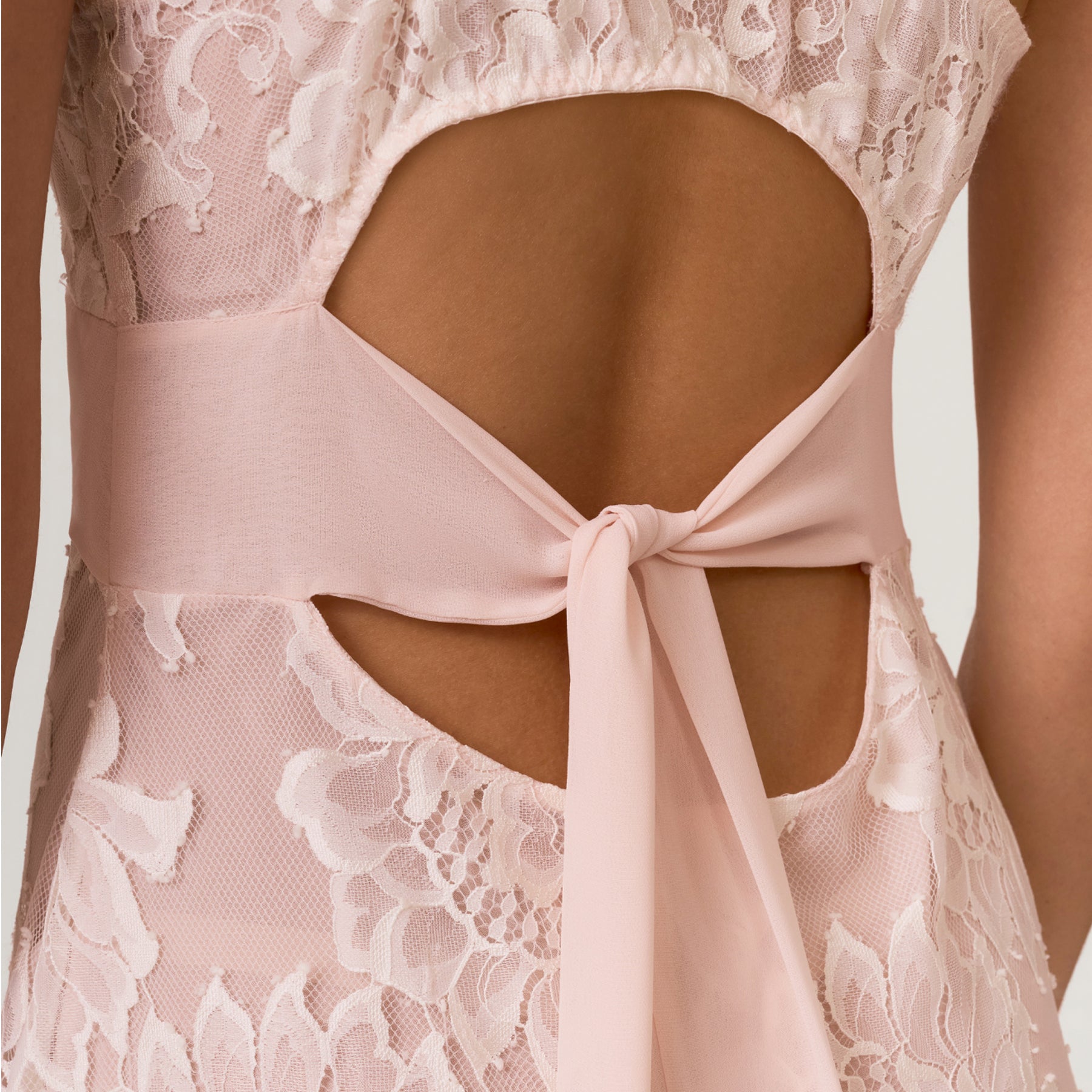 Close-up of open-back detail on blush lace bridal gown with sheer lace panels and chiffon waist tie.