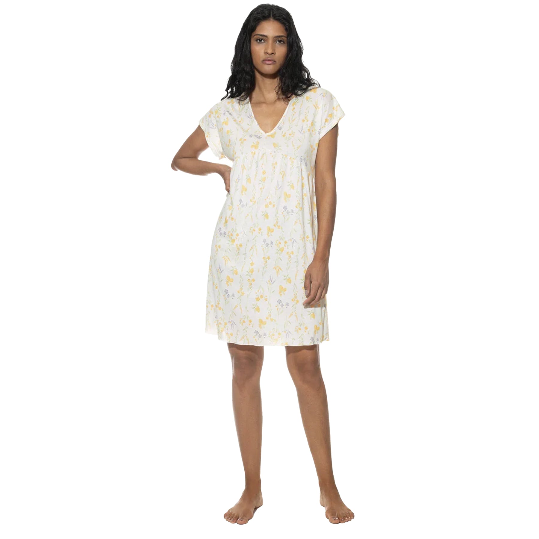 Woman wearing a short-sleeved, V-neck white nightdress with a yellow and lavender floral print, standing with one hand on her hip