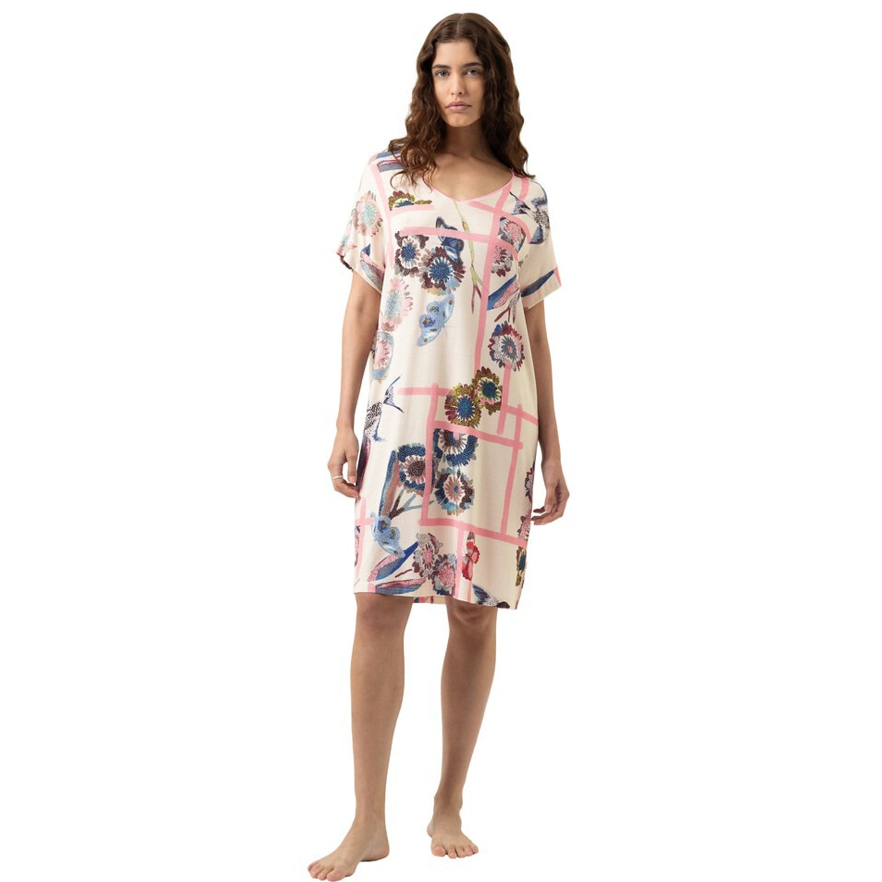 Woman wearing a knee-length short-sleeve nightdress with a soft cream base and fragmented garden floral print in pink, blue, and earthy tones, front view on a white background.