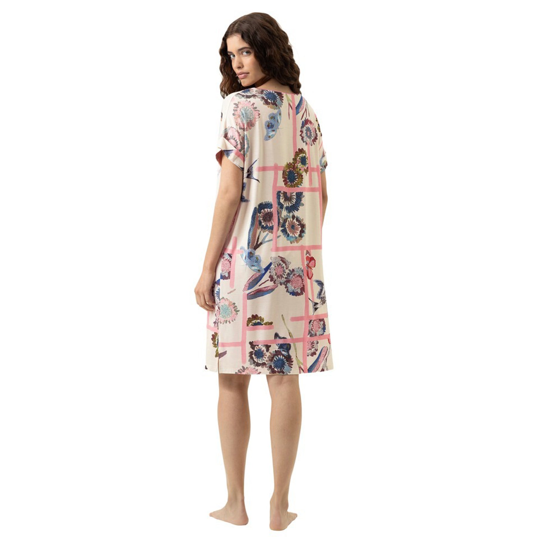 Back view of a woman wearing a relaxed knee-length nightdress with a cream base and fragmented garden floral print, short sleeves and easy silhouette.