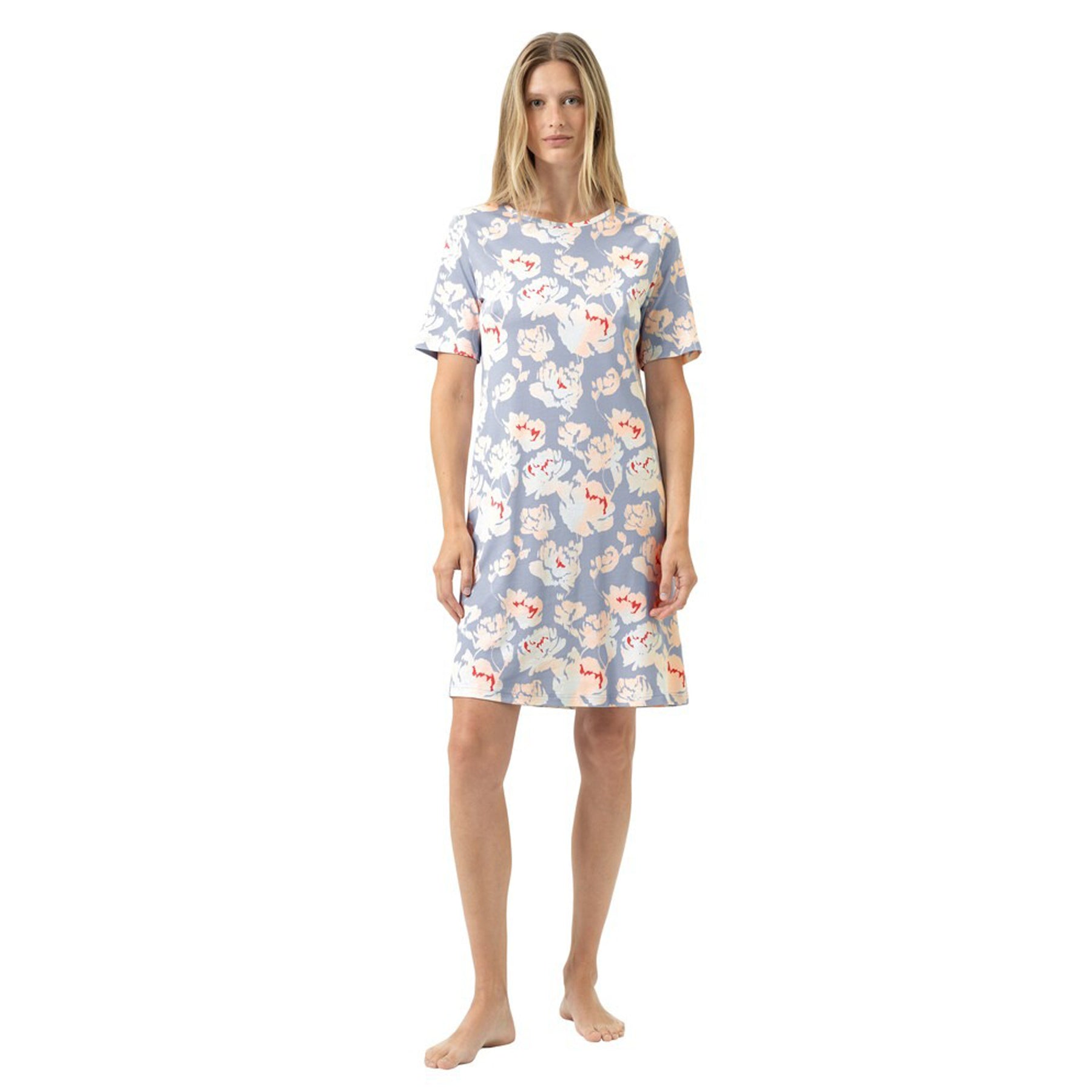 Woman wearing a short-sleeve floral nightdress with a soft blue background and light peach-and-ivory flower print, knee-length fit, front view.