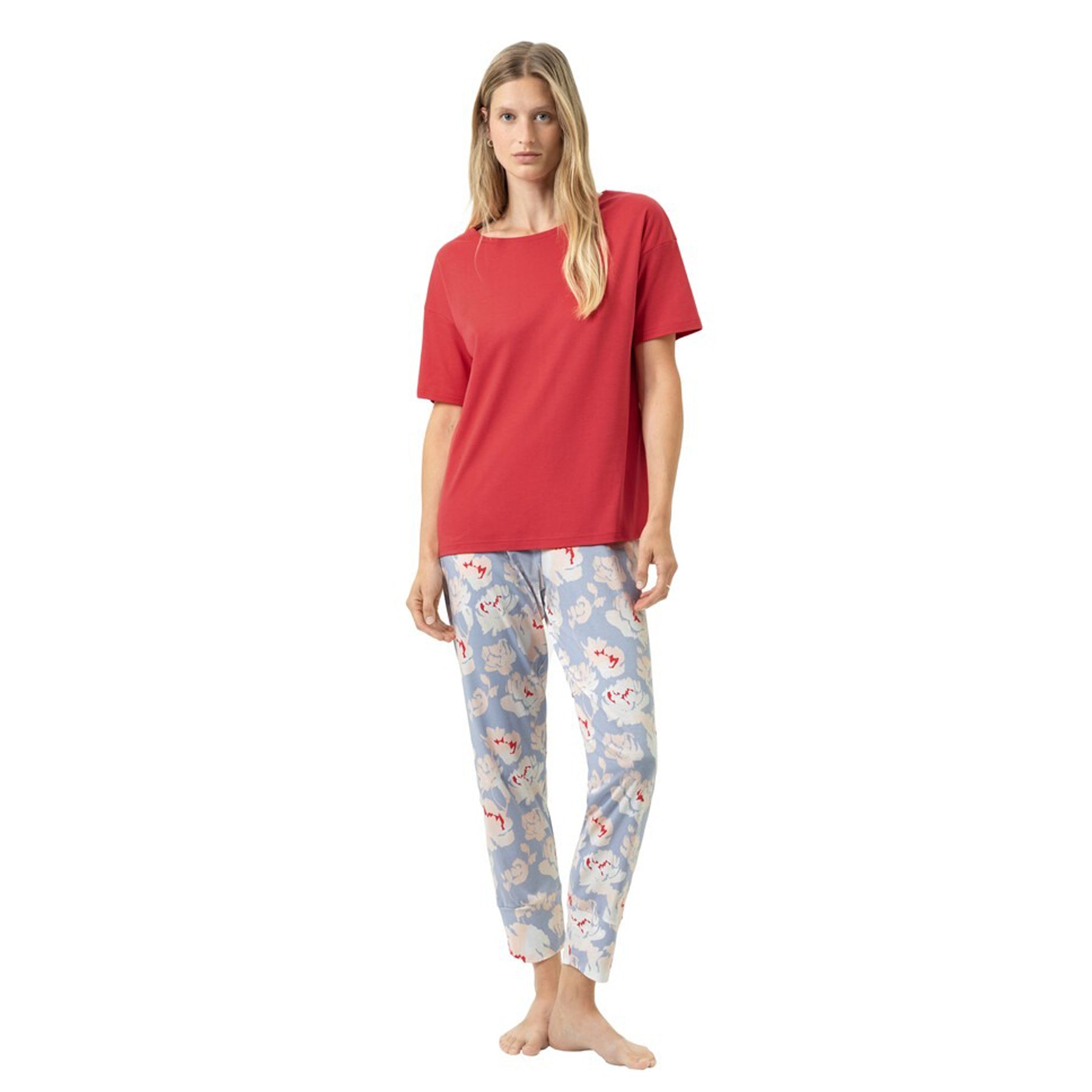 Woman wearing a short-sleeve red pyjama top with soft blue floral print pyjama pants, relaxed fit, front view on a white background.