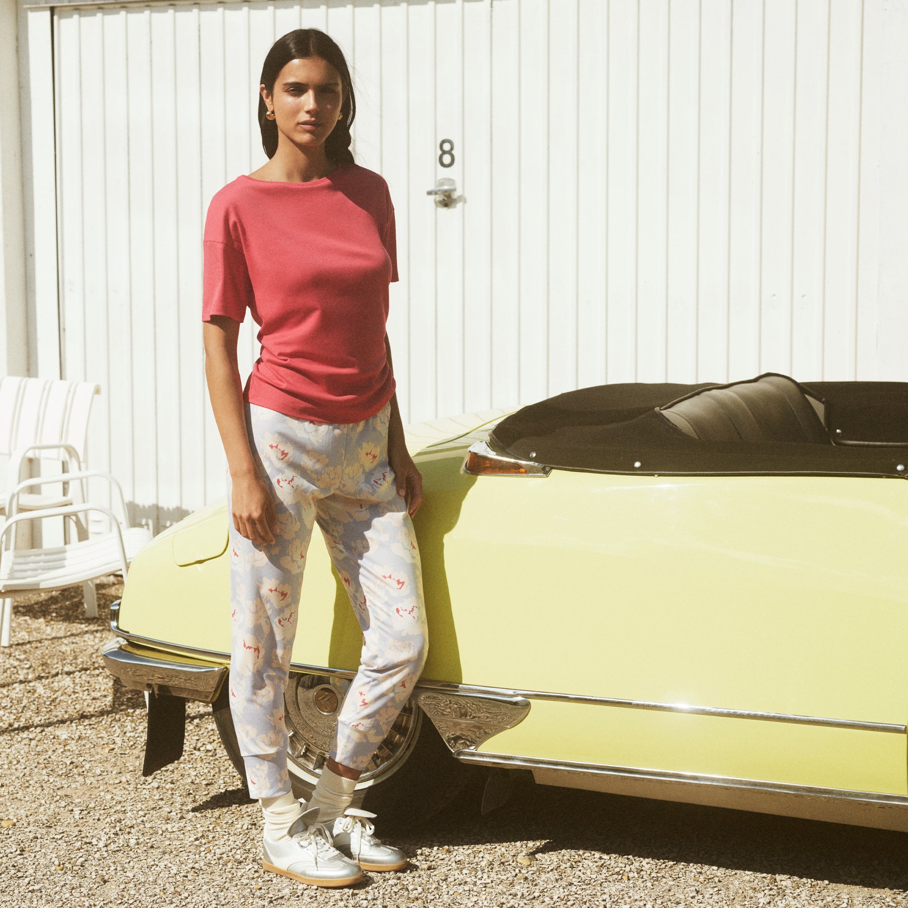 Woman wearing a red short-sleeve pyjama top and soft blue floral print pyjama pants, styled casually outdoors beside a vintage car.