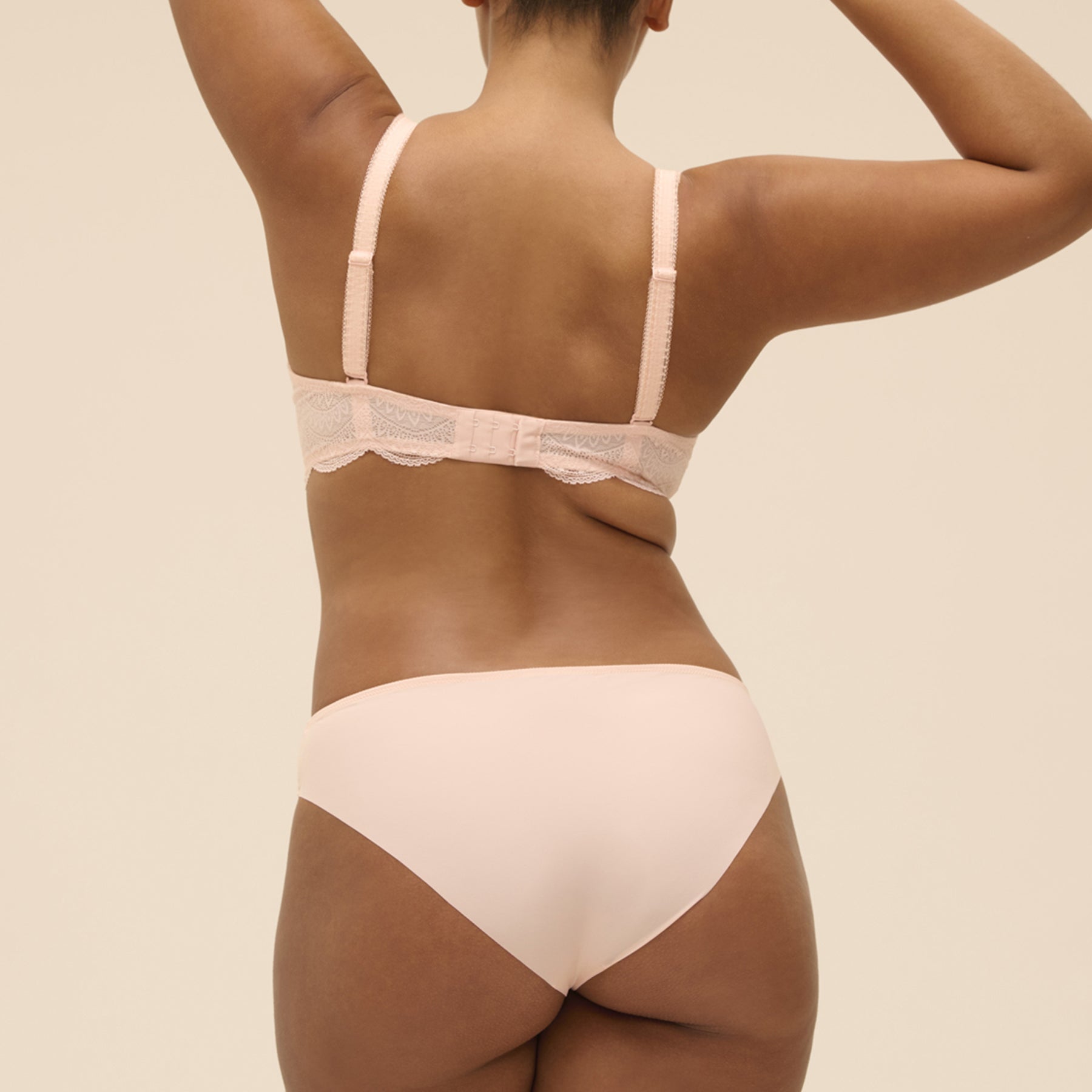 Back view of blush pink lace bra with wide adjustable straps and seamless high-cut panty, shown on a fuller-bust model.