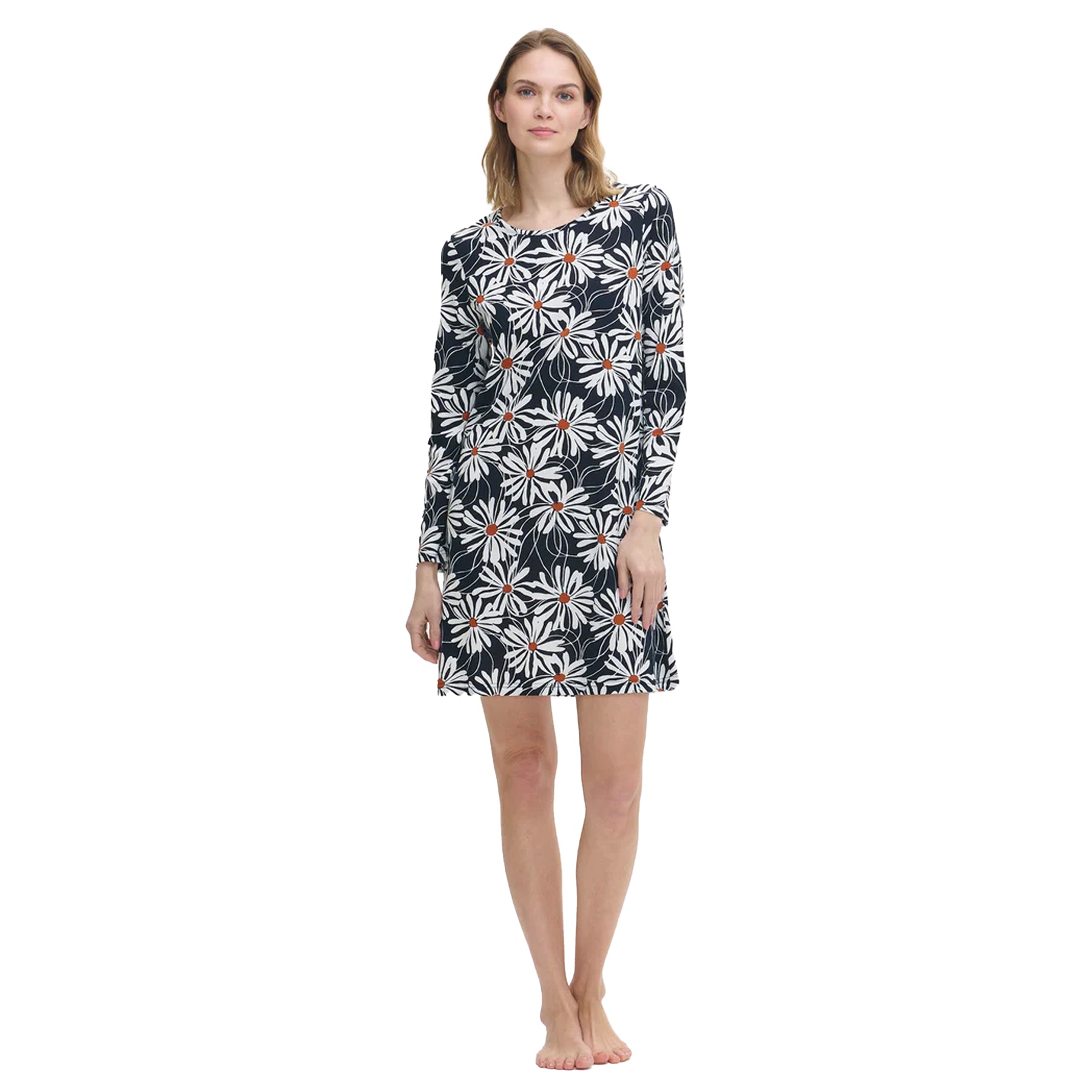 Woman wearing a long-sleeve navy nightdress with large white daisy print and orange centres, standing barefoot against a white background.