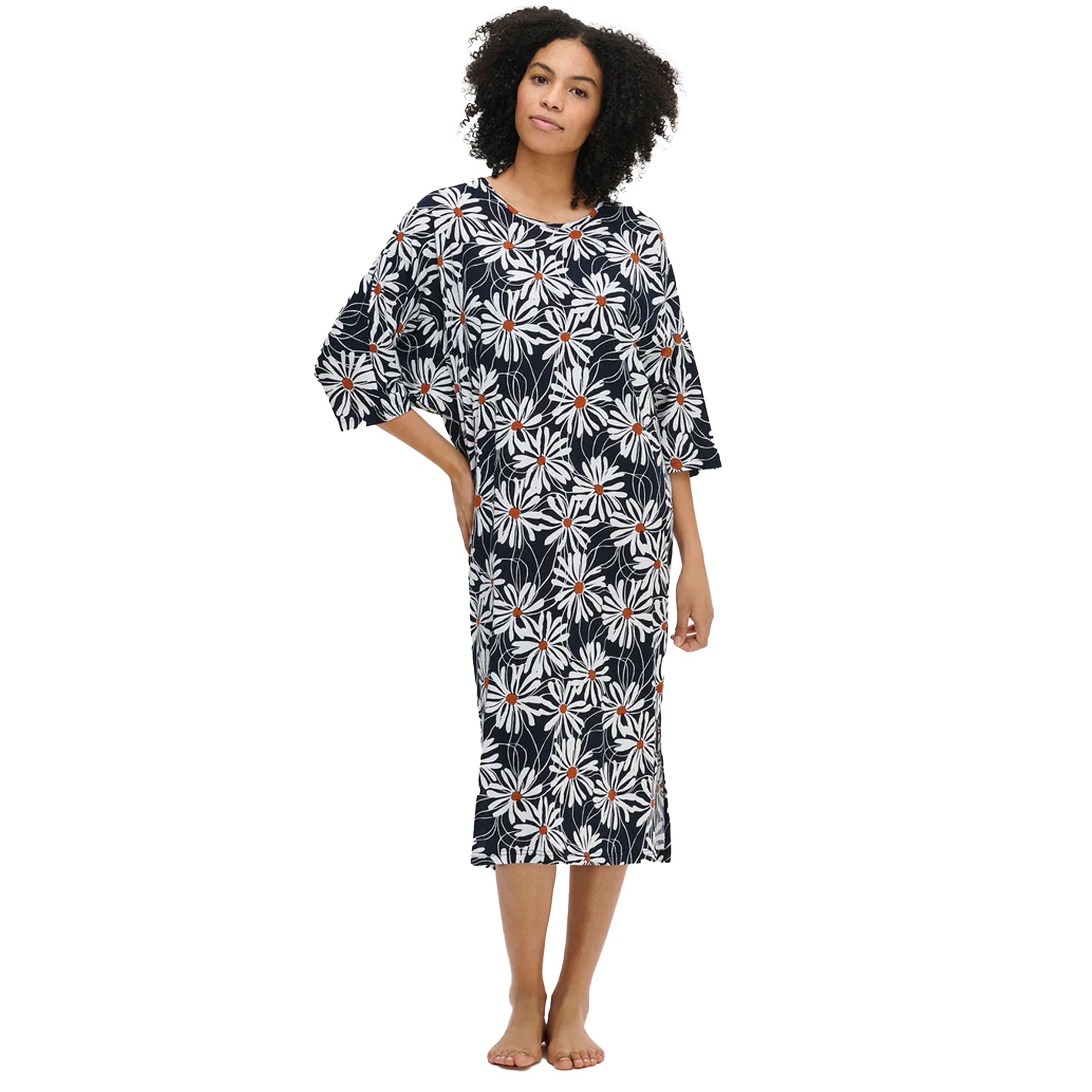 Woman wearing a navy nightdress with white daisy floral print and orange centres, featuring elbow-length sleeves and side slits, standing barefoot against a white background.