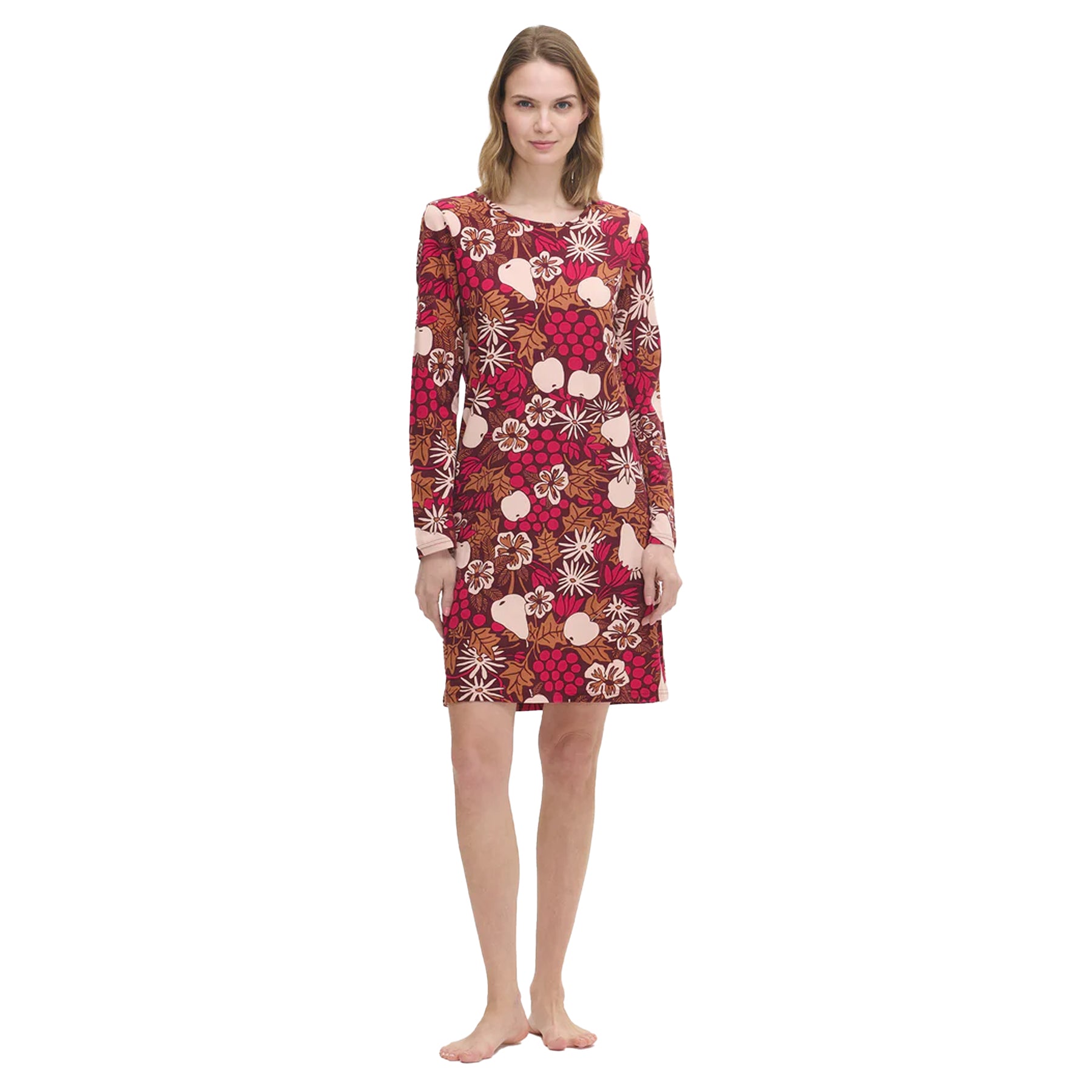Woman wearing a long-sleeve burgundy nightdress with a colourful fruit and floral print, standing barefoot against a white background.