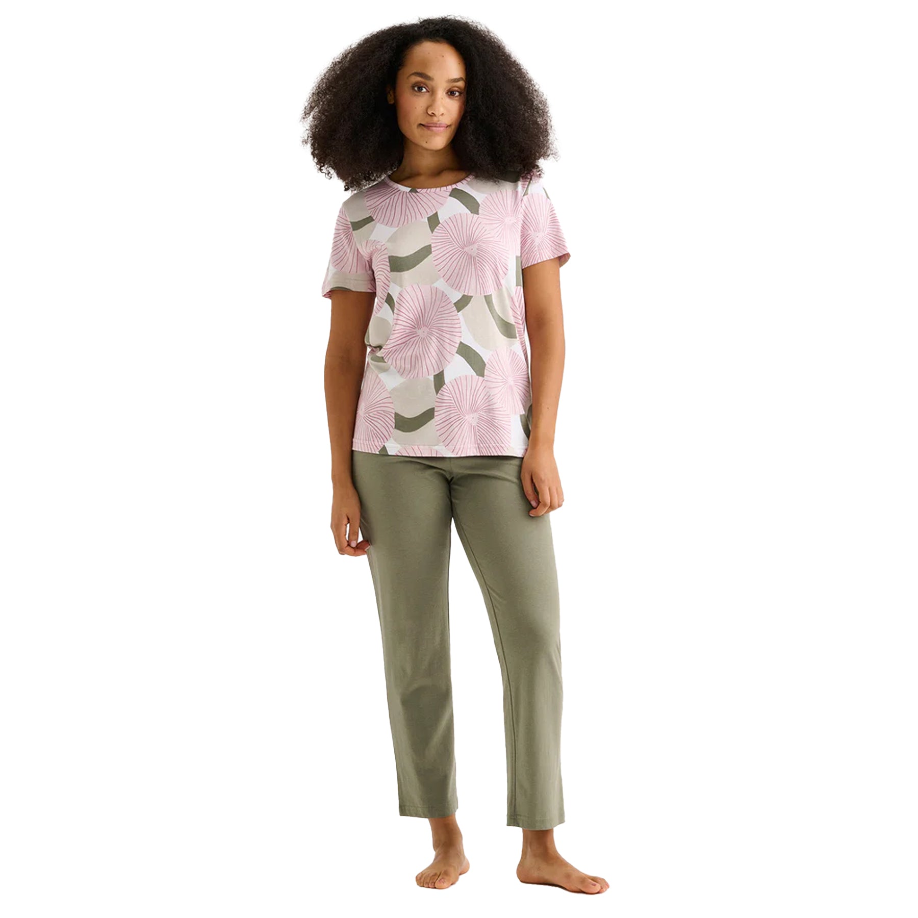 Woman wearing a pink circular floral print short-sleeve pajama top with solid sage green lounge pants.