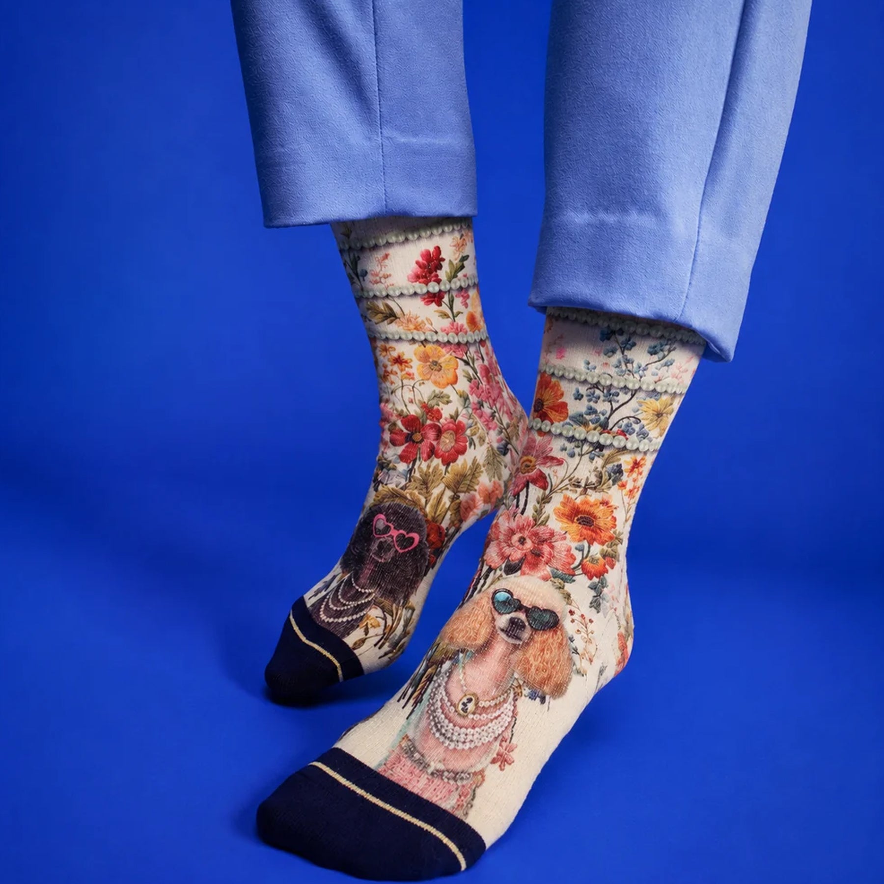 Model wearing floral crew socks featuring stylish poodles in sunglasses and pearl details against a bright blue background.