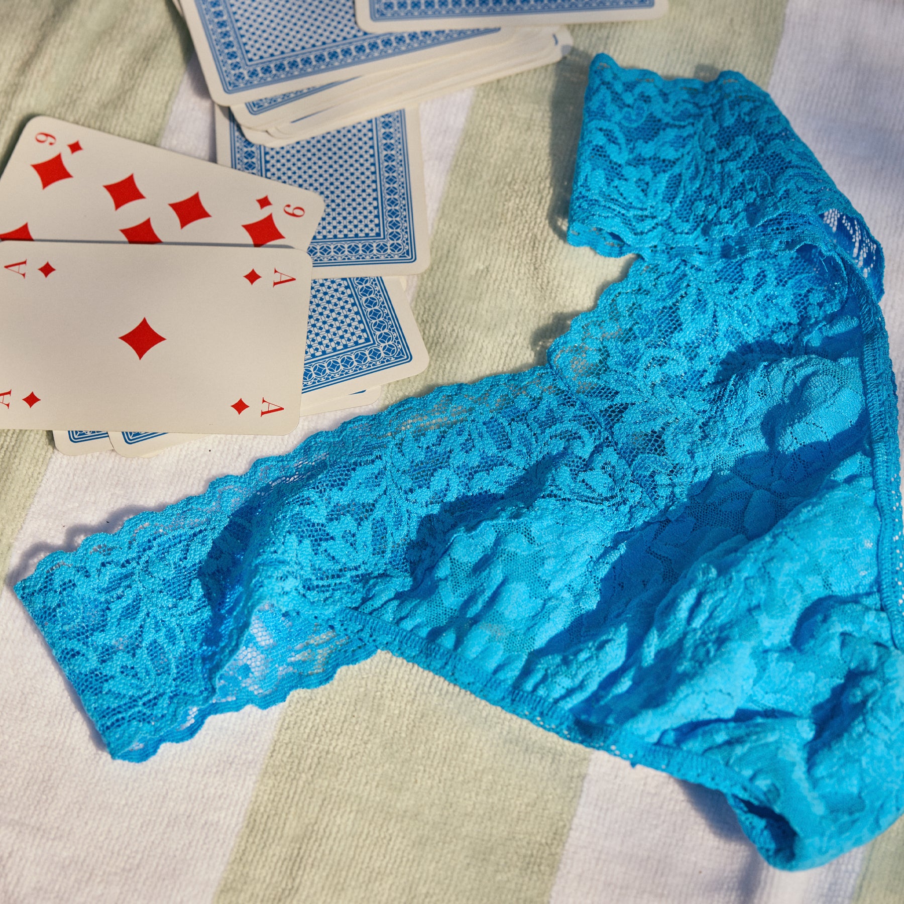 Blue lace thong underwear styled on towel with playing cards, floral stretch lace waistband