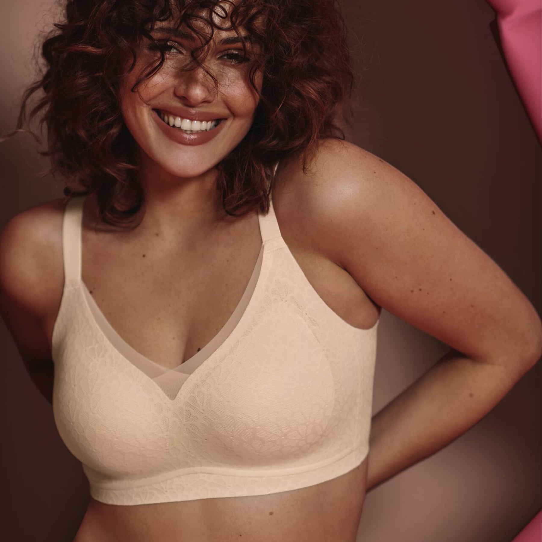 Smiling woman wearing a wireless beige lace bra with soft cups and mesh neckline detail, close-up lifestyle image