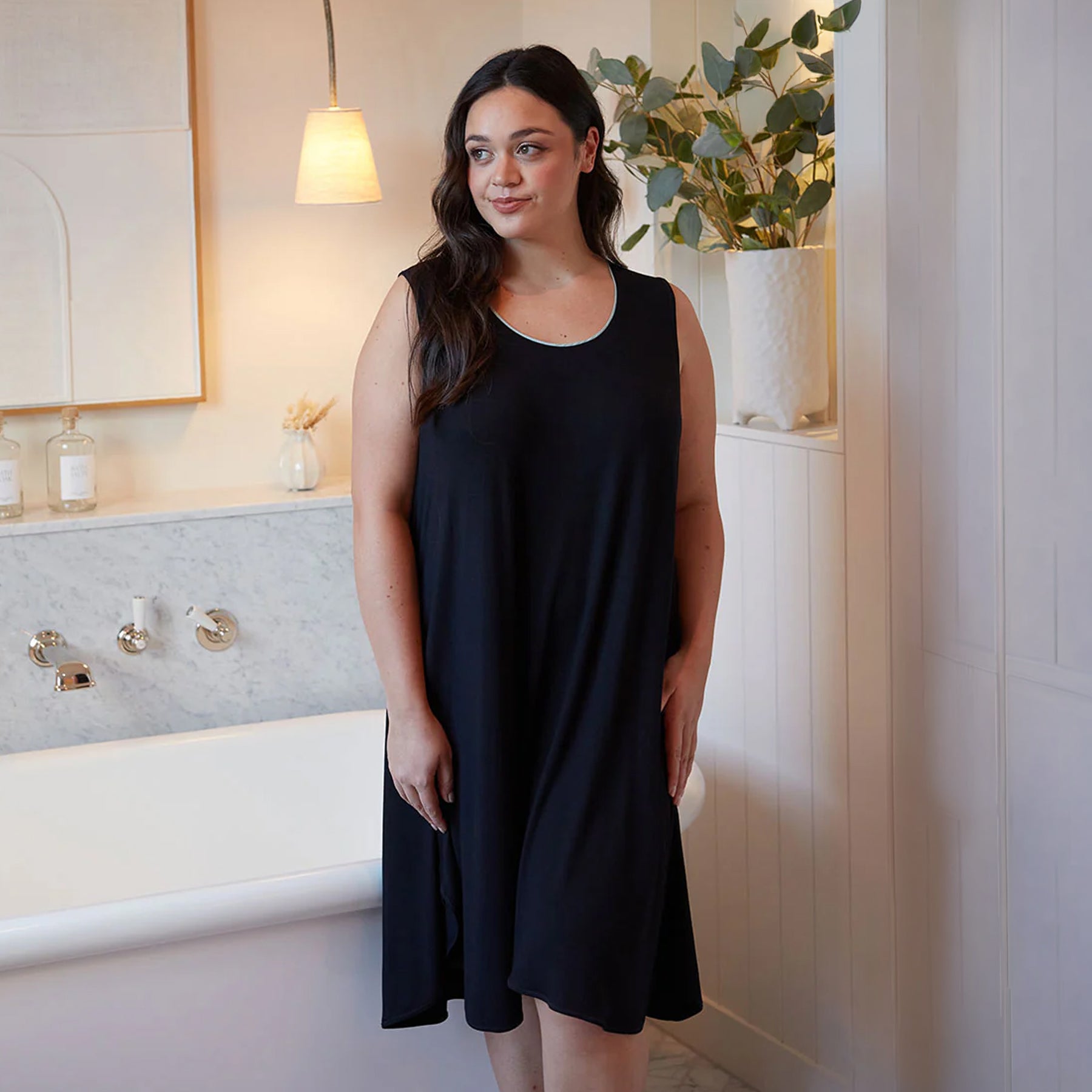 Woman wearing a black sleeveless jersey nightgown with relaxed flowing silhouette, scoop neckline and contrast trim detail.