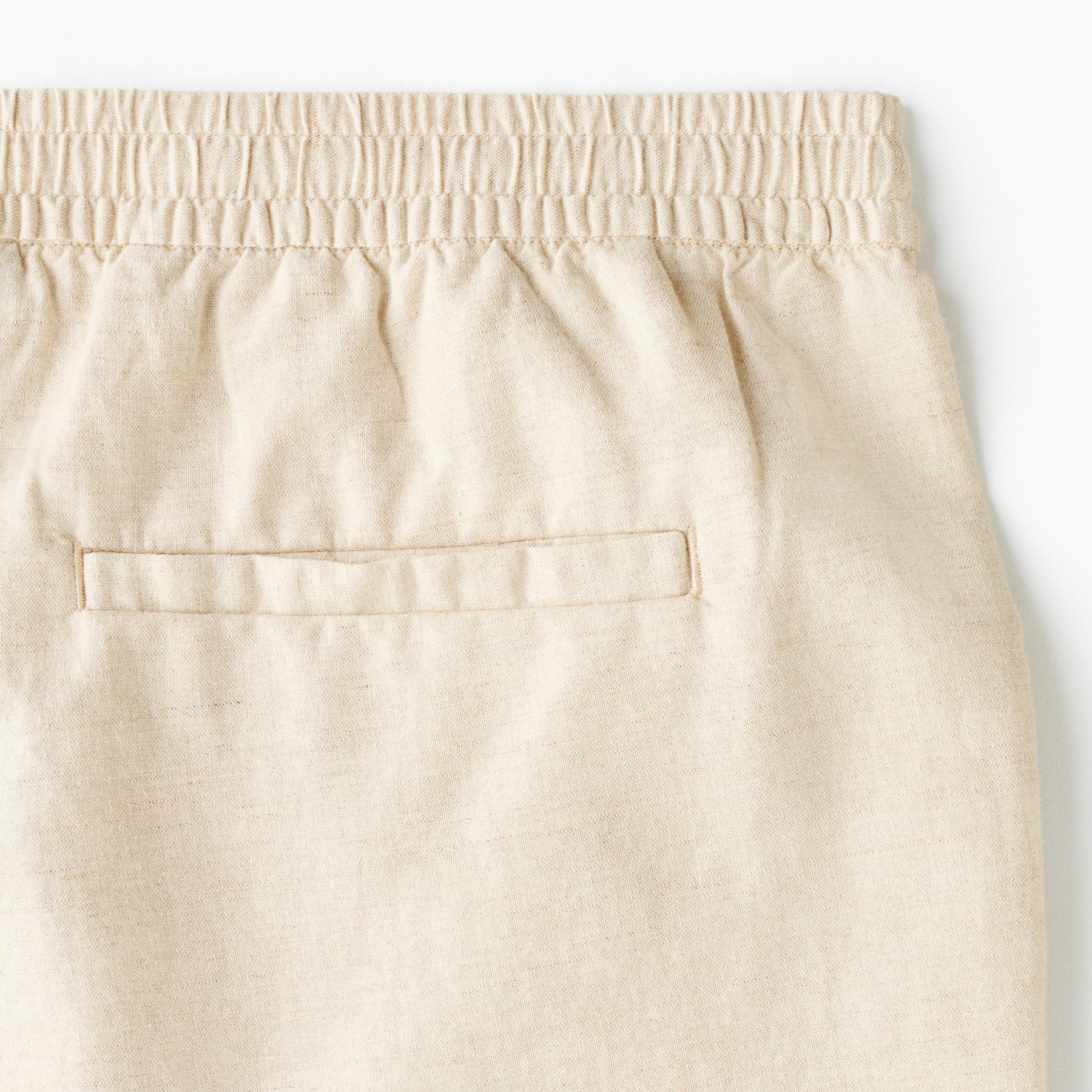 Close-up of beige linen shorts back welt pocket and elastic waistband detail.