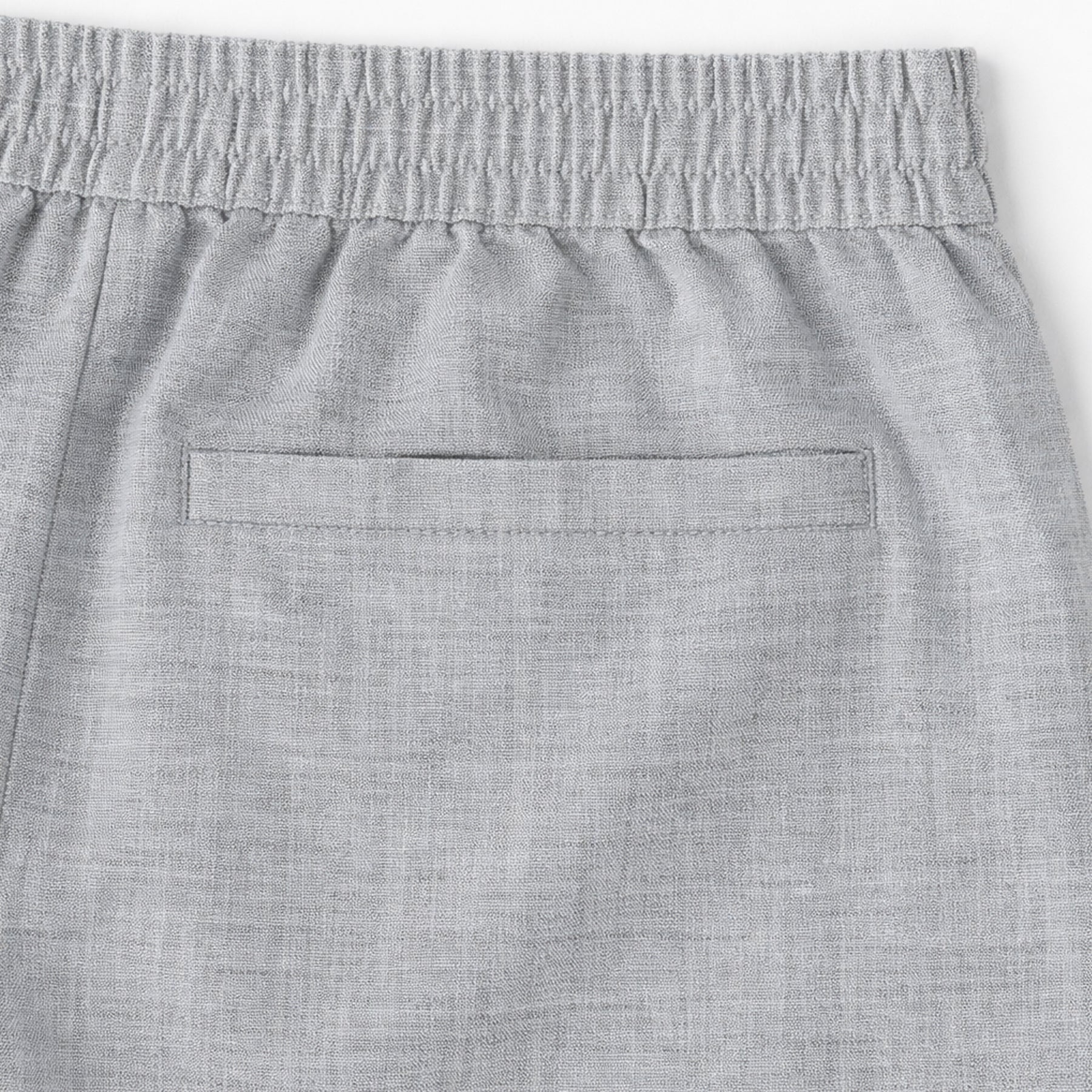 Close-up of light grey linen shorts back welt pocket and elastic waistband detail.