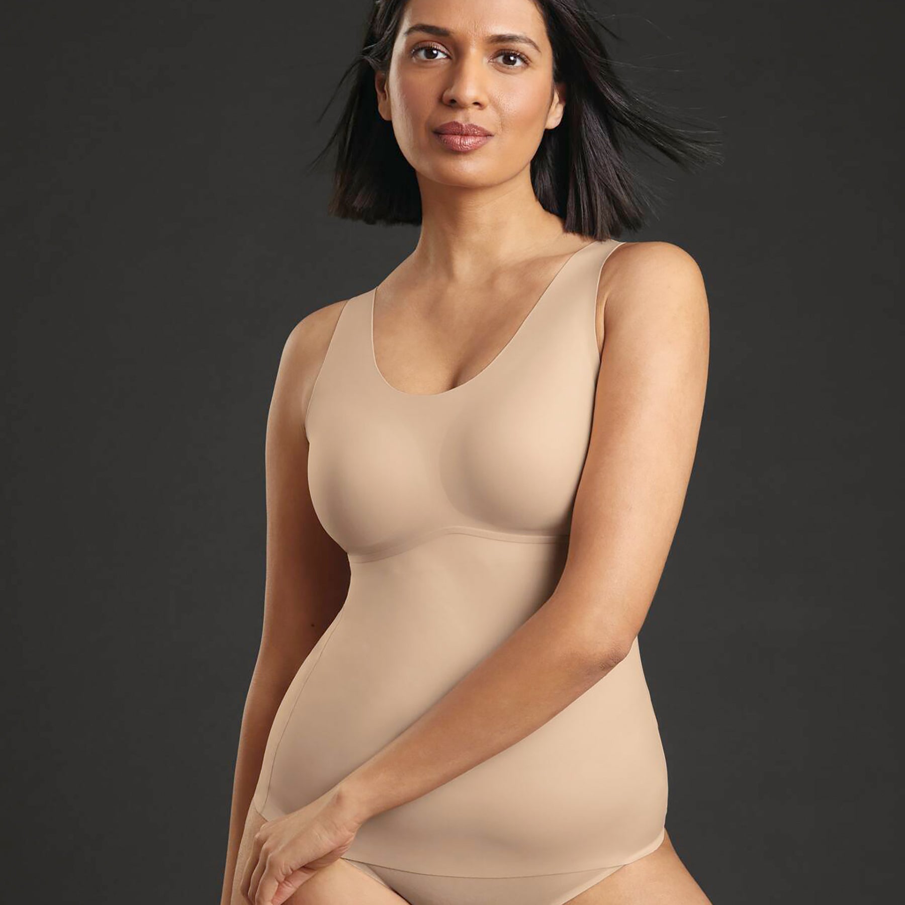 Woman wearing ANITA 0654 Essential Tank with Shelf Bra in Desert nude, lifting hem to show soft stretch fabric