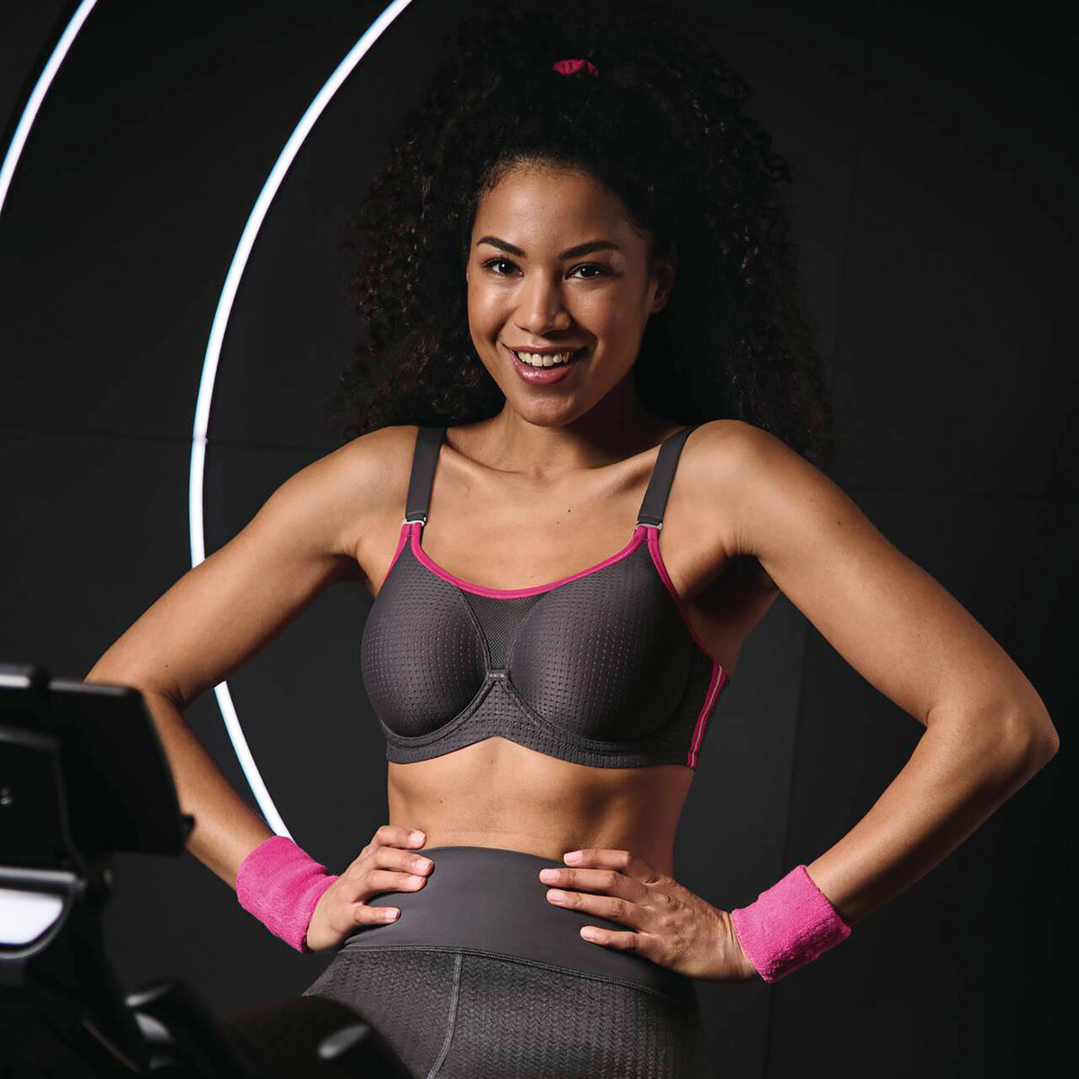Anita 5599 performance wireX sports bra in 481 anthrazit/pink; a charcoal grey with hot pink trim. Front view on model working out on a bike.