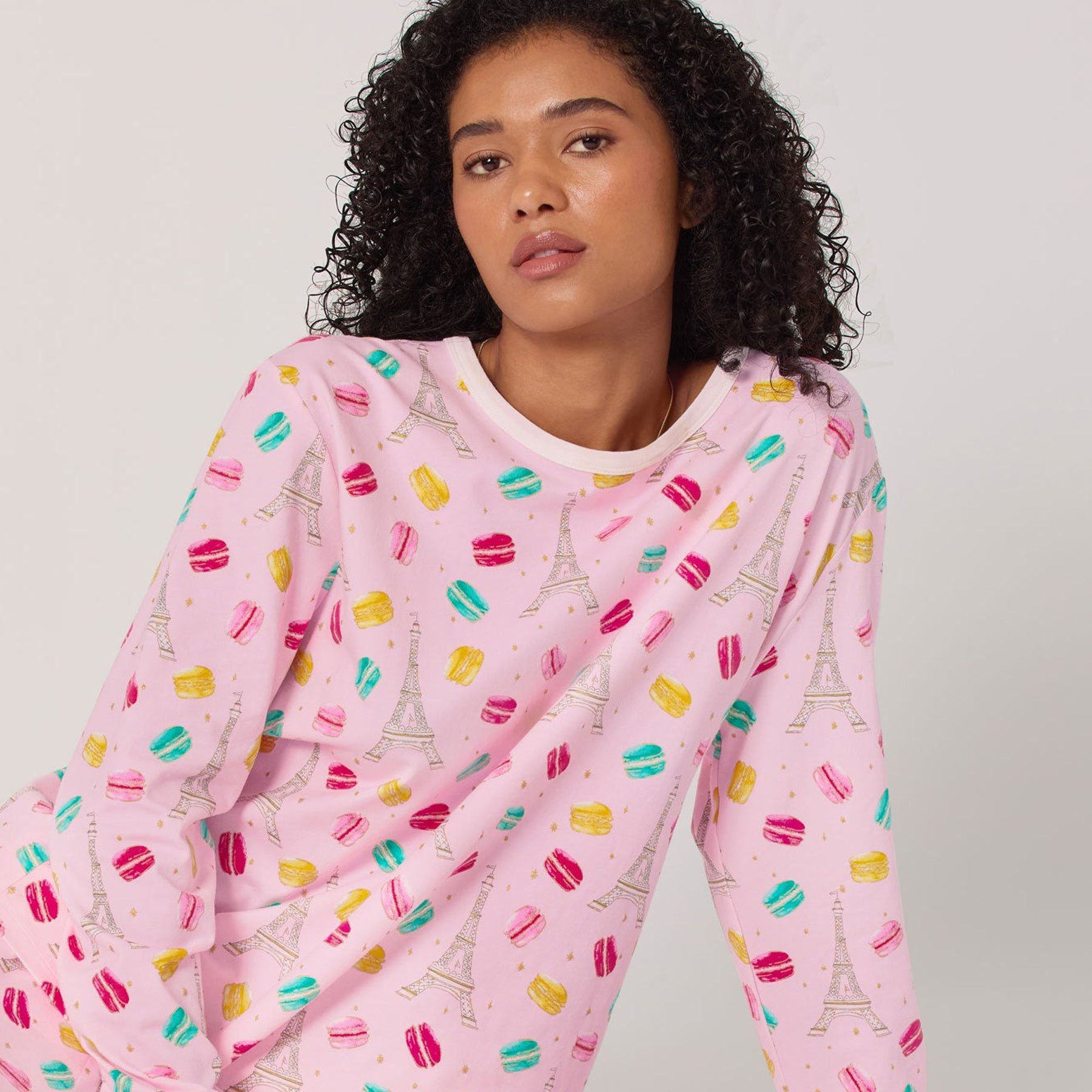 Person wearing a pink pajama set with Eiffel Tower and macaron designs on a plain background