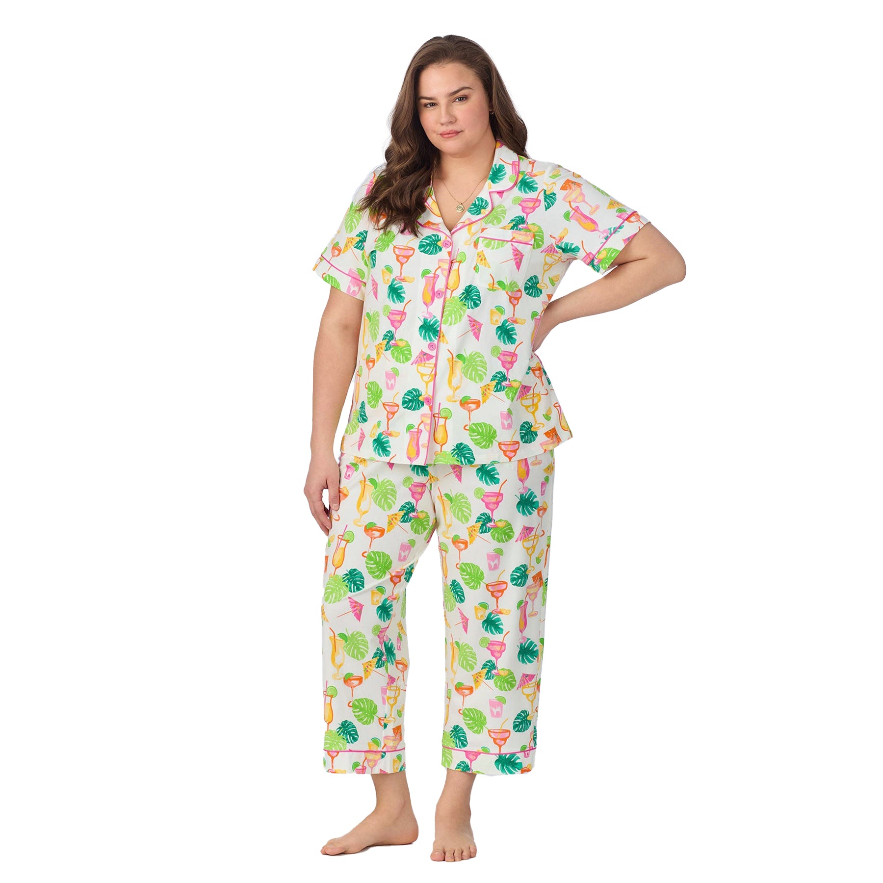 Plus-size model posing in front view wearing a vibrant printed pyjama set with cocktails and palm leaves.