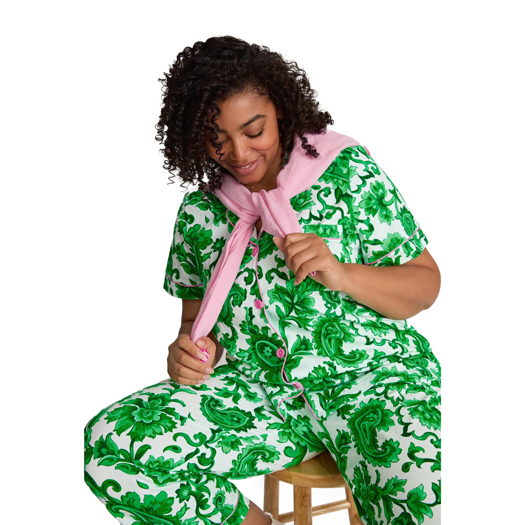 Woman wearing a green floral print pyjama set with pink piping details and relaxed lounge styling.