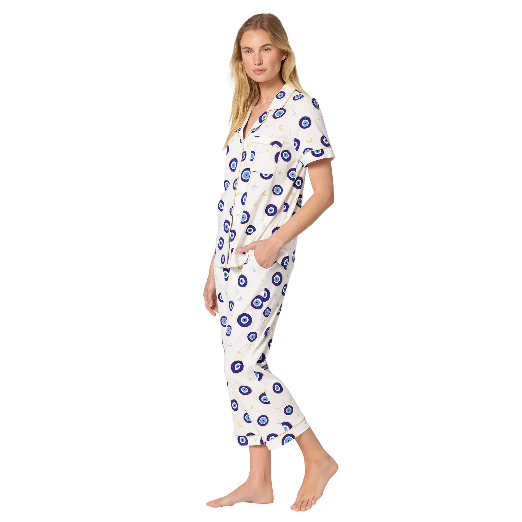 Side view of an ivory short-sleeve pajama set with blue evil eye celestial print, cropped pants and contrast gold piping.