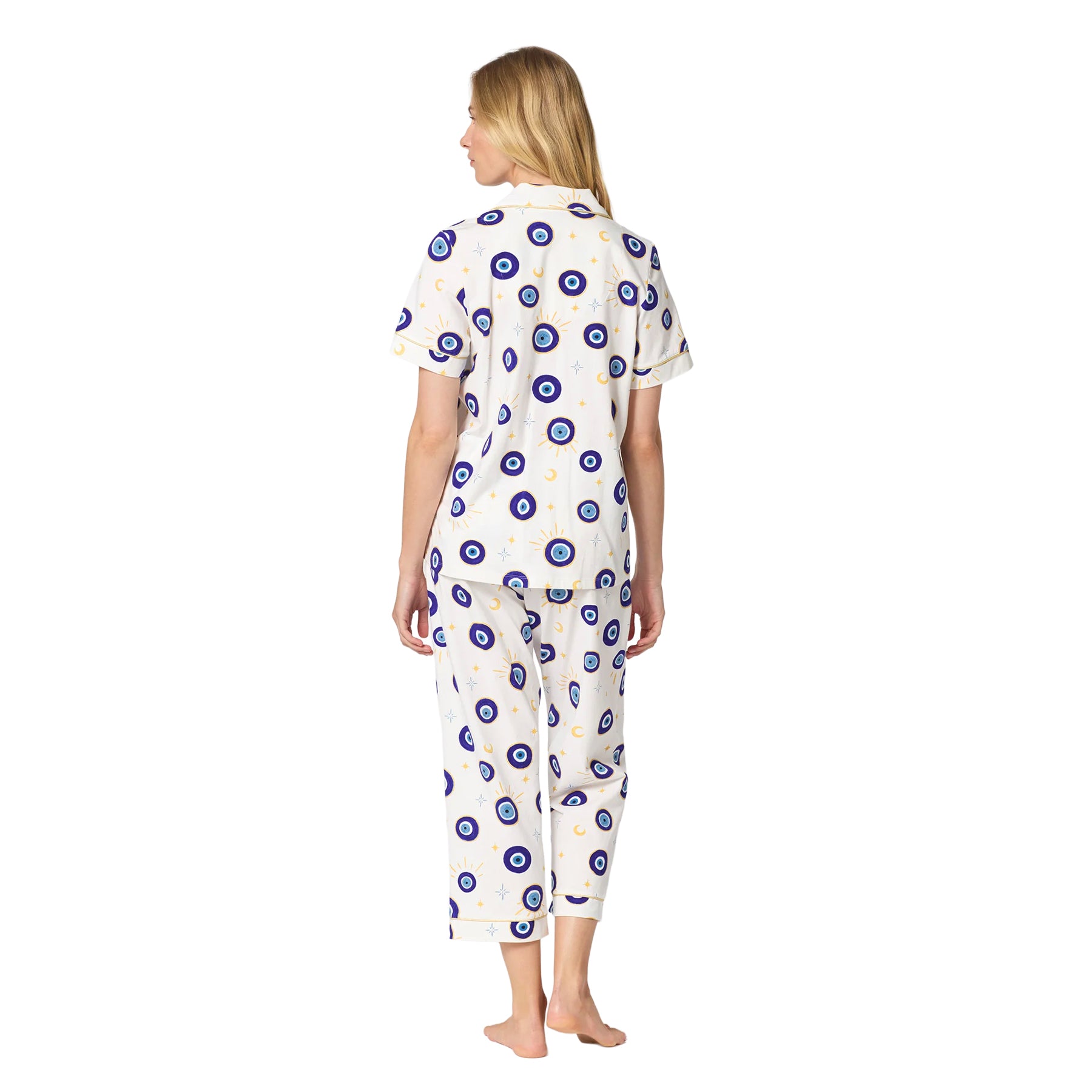 Back view of an ivory short-sleeve pajama set with cropped pants, blue evil eye, moon and star print, and gold piping.