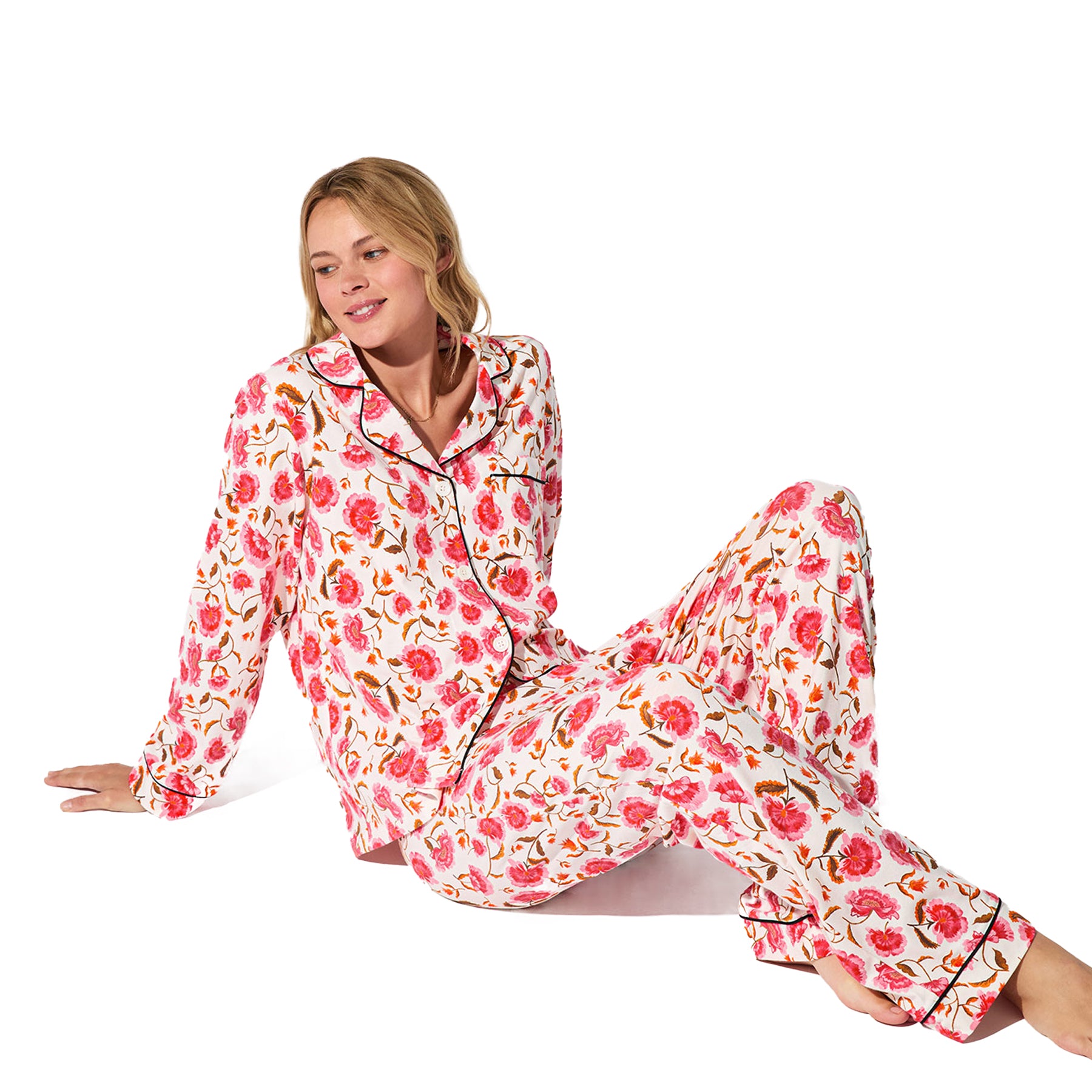 Woman sitting in white floral pyjama set with bright floral pattern and contrast piping.