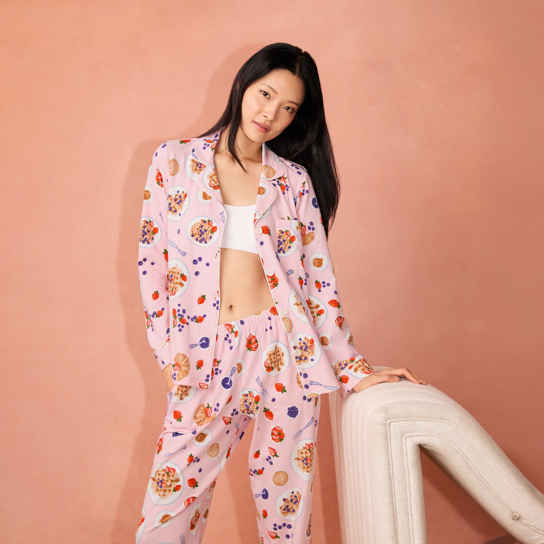 Woman in pink waffle brunch pyjamas with open shirt styled over a white bralette, lifestyle setting.
