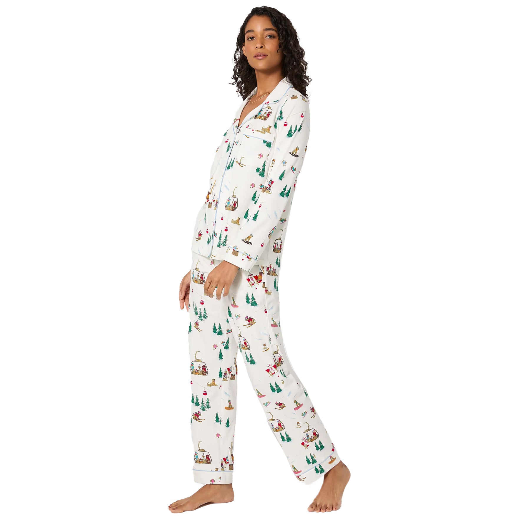 Side view of woman in festive white pyjama set with playful ski-themed print and blue piping.
