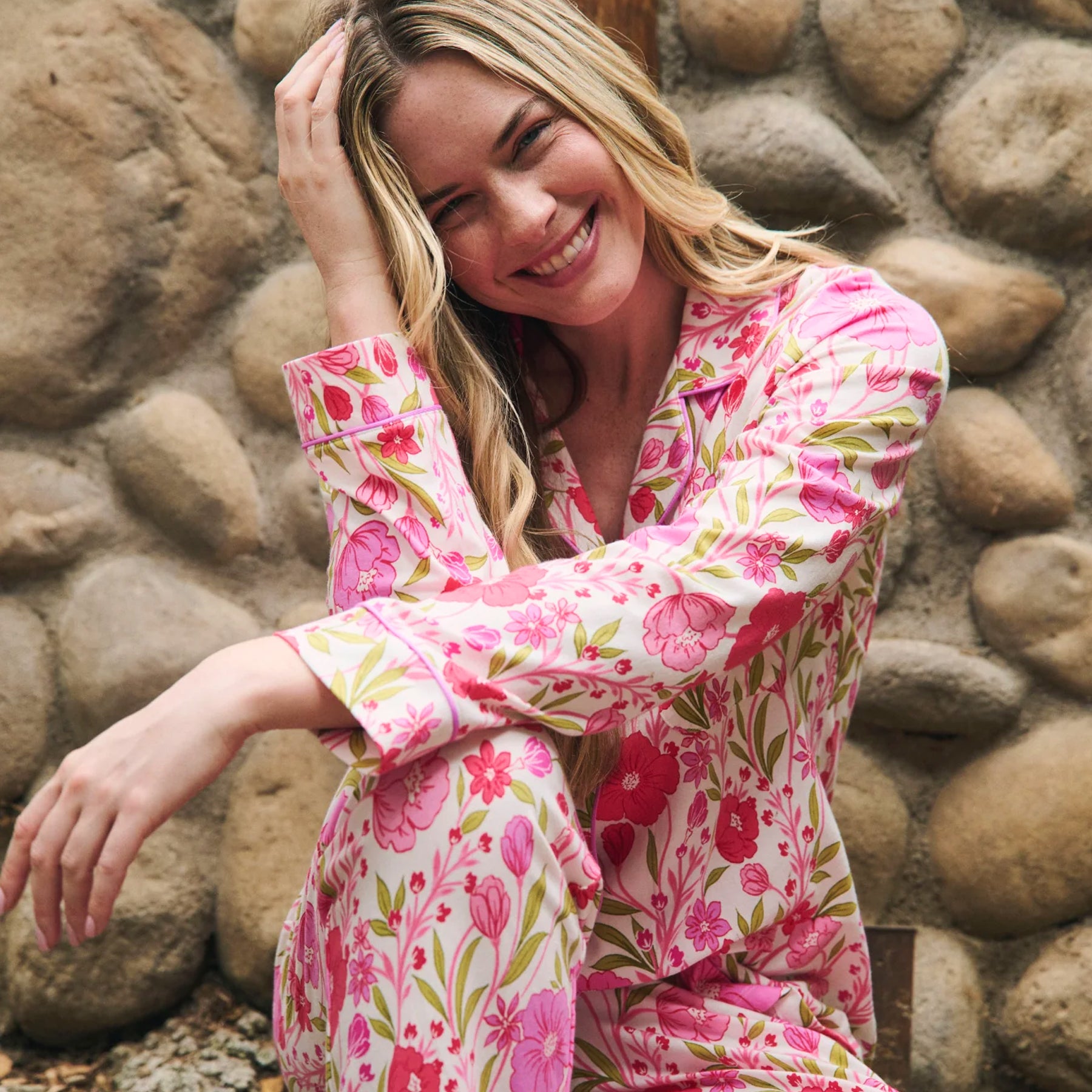 Woman wearing a white long-sleeve pajama set with vibrant pink floral print and green leaves, seated outdoors.