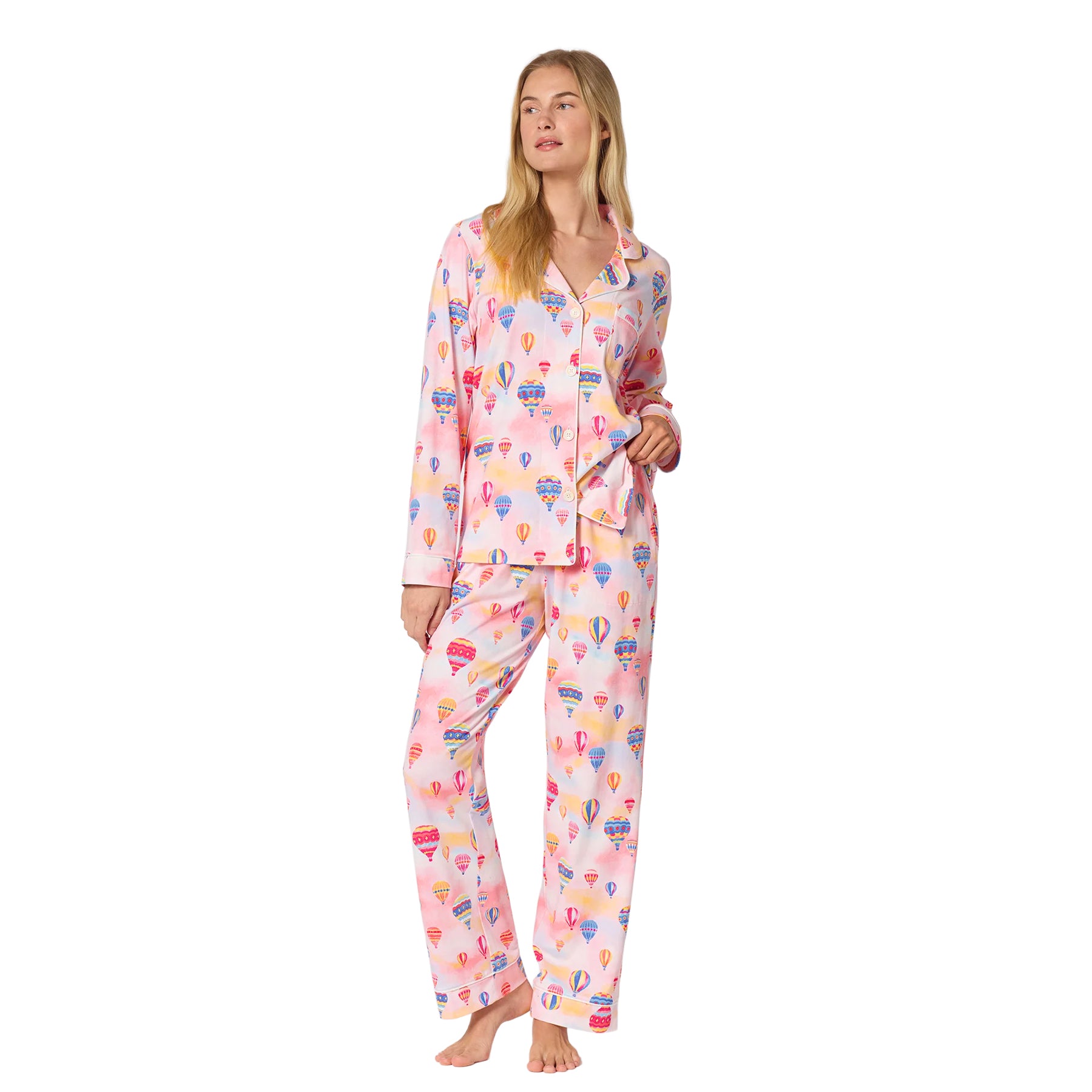 Woman wearing a pink long-sleeve pajama set with colourful hot air balloon print, button-front top and full-length pants.