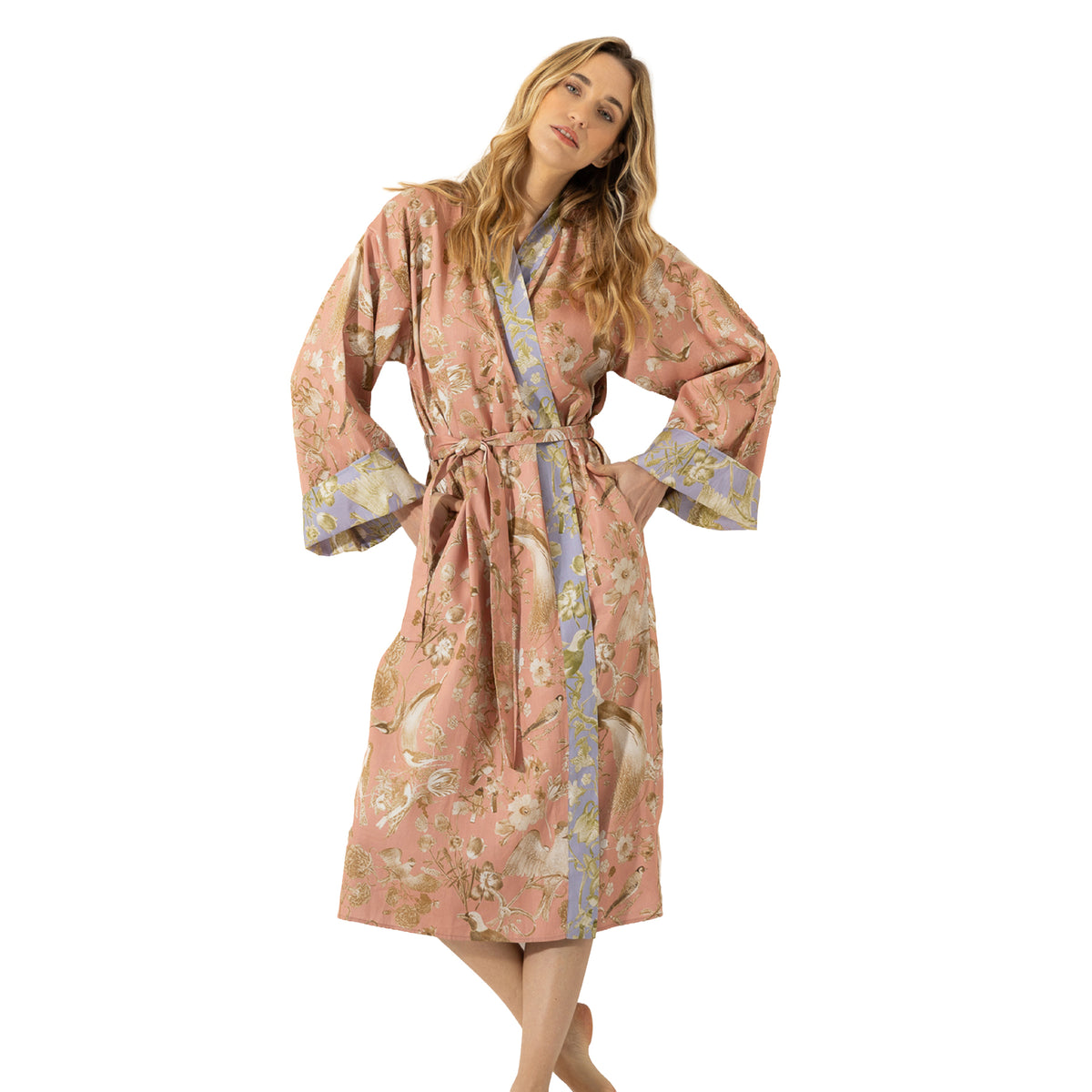 Woman modelling a long dusty pink floral robe with bird print, lavender contrast trim, wide sleeves and a matching tie belt.