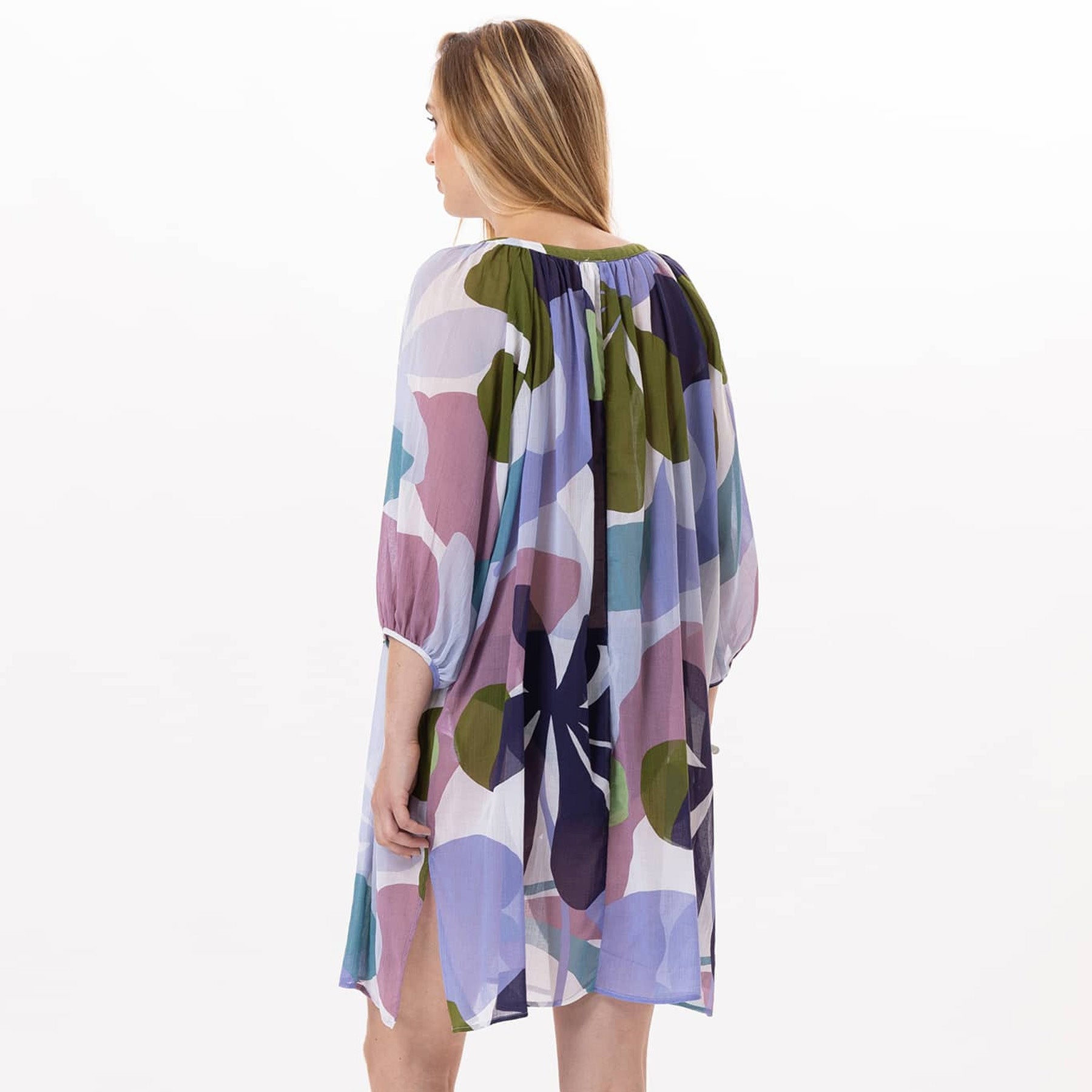 Back view of a woman wearing a loose, multicolour floral dress with gathered fabric at the neckline and sleeves, showing its relaxed, airy fit.