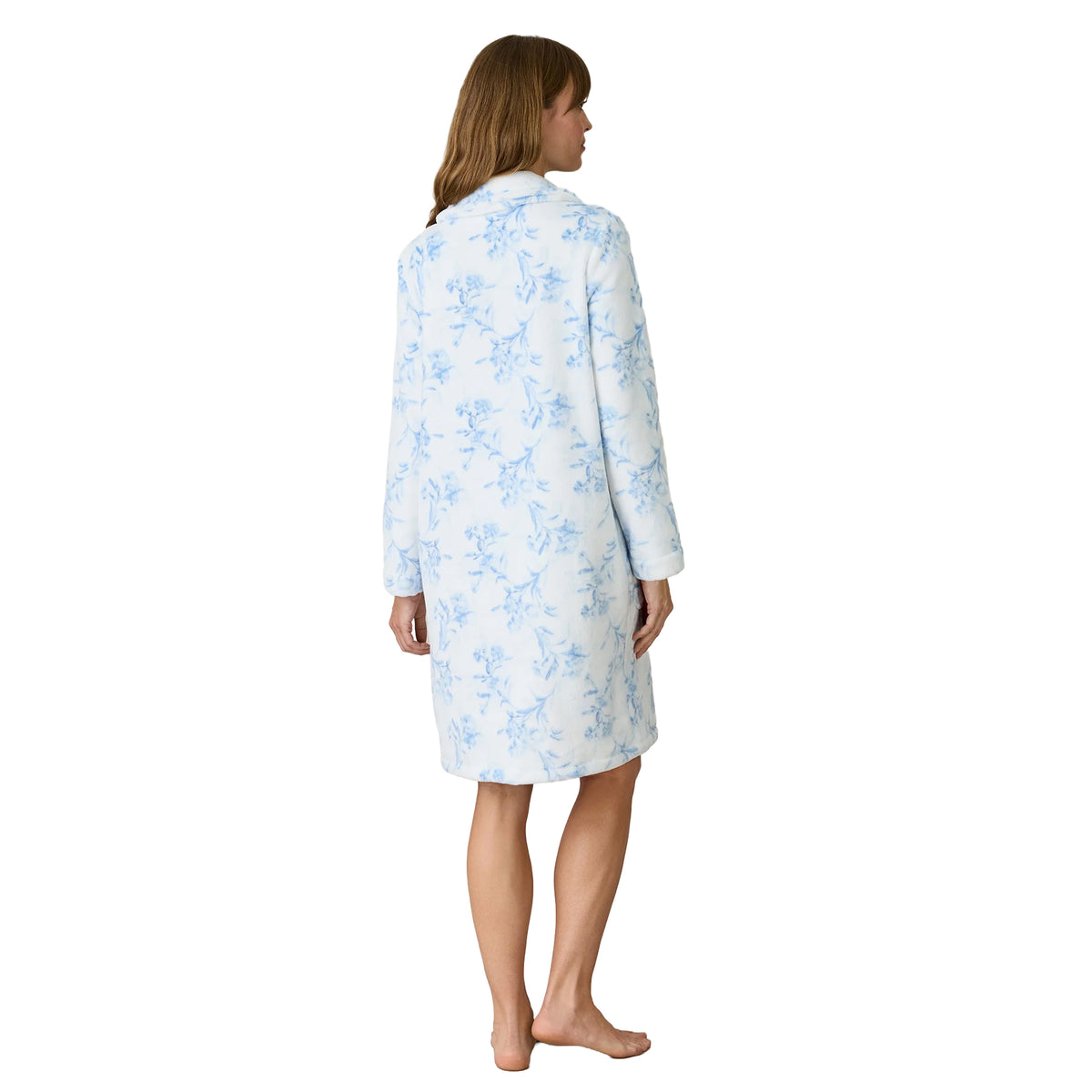 Back view of a woman wearing a knee-length white fleece robe with a light blue floral print, relaxed silhouette, long sleeves and fold-over collar.