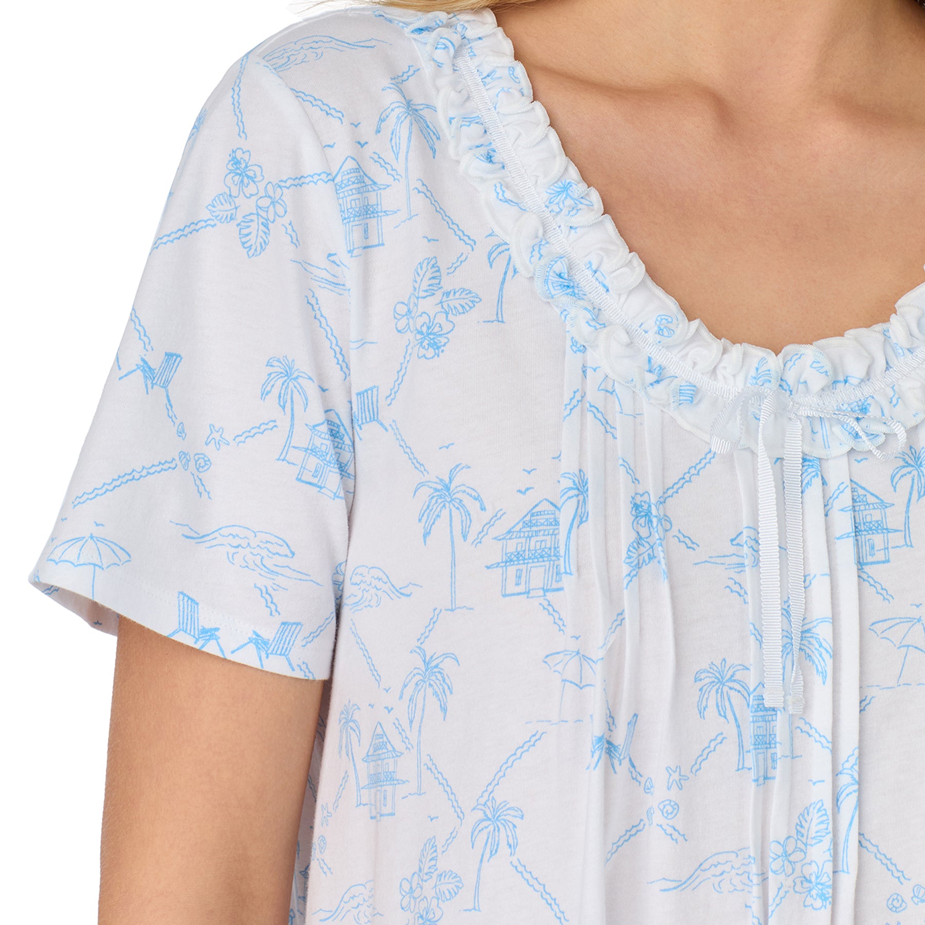 Close-up of the neckline and shoulder, highlighting the ruffle trim and blue beach cottage and palm tree print.