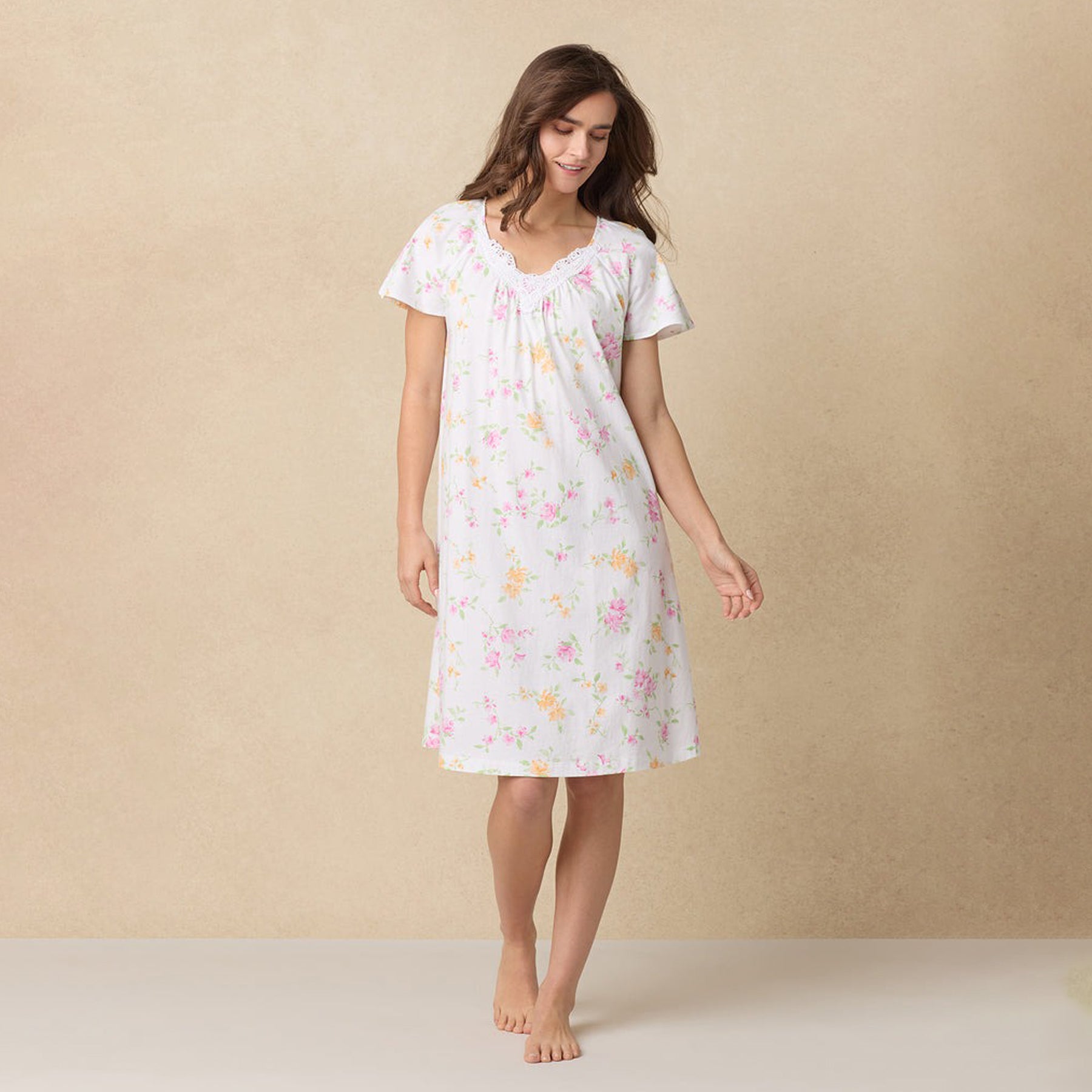 Woman in a white floral nightgown looking down, standing against a neutral background.