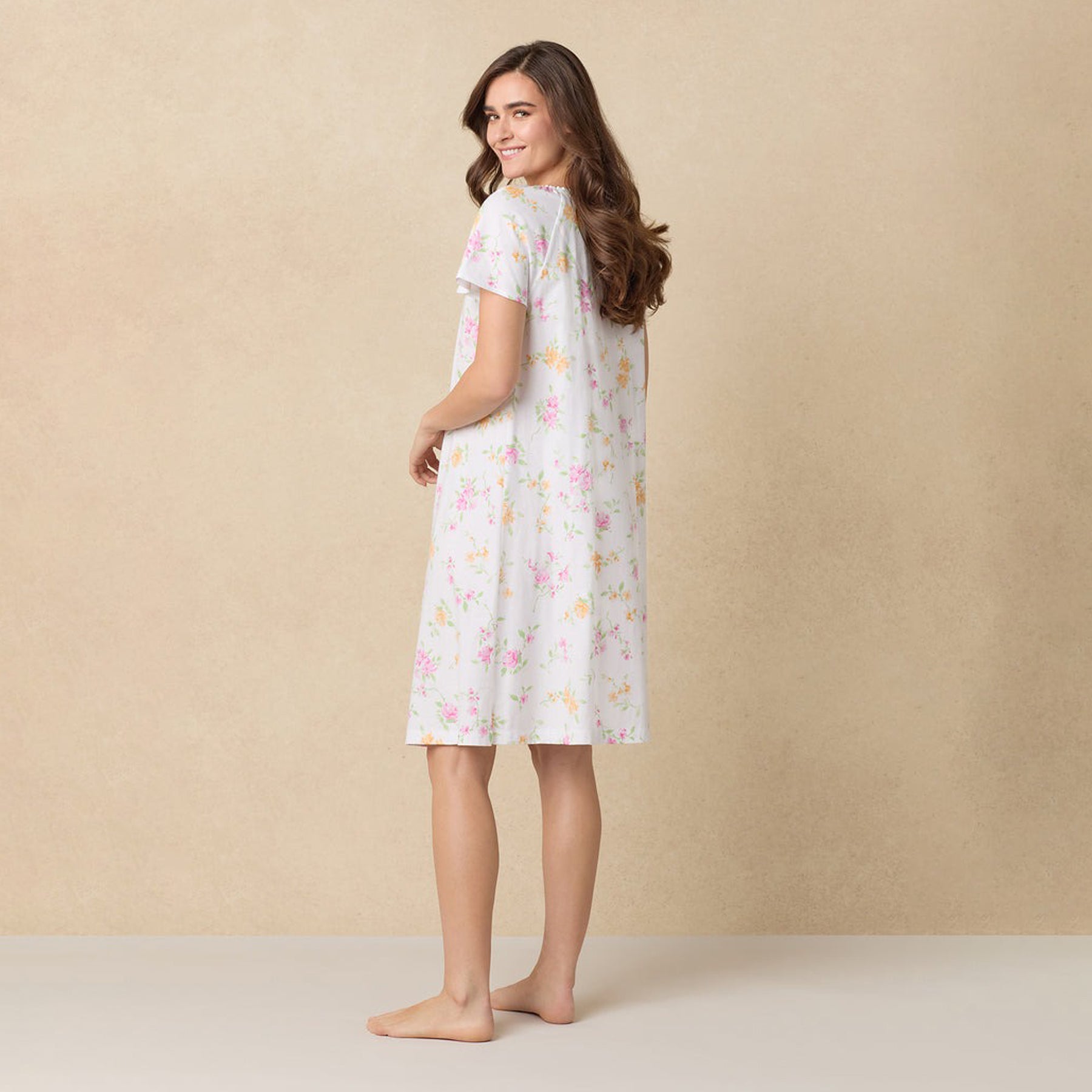 Back view of a woman wearing a knee-length floral nightgown with short sleeves.