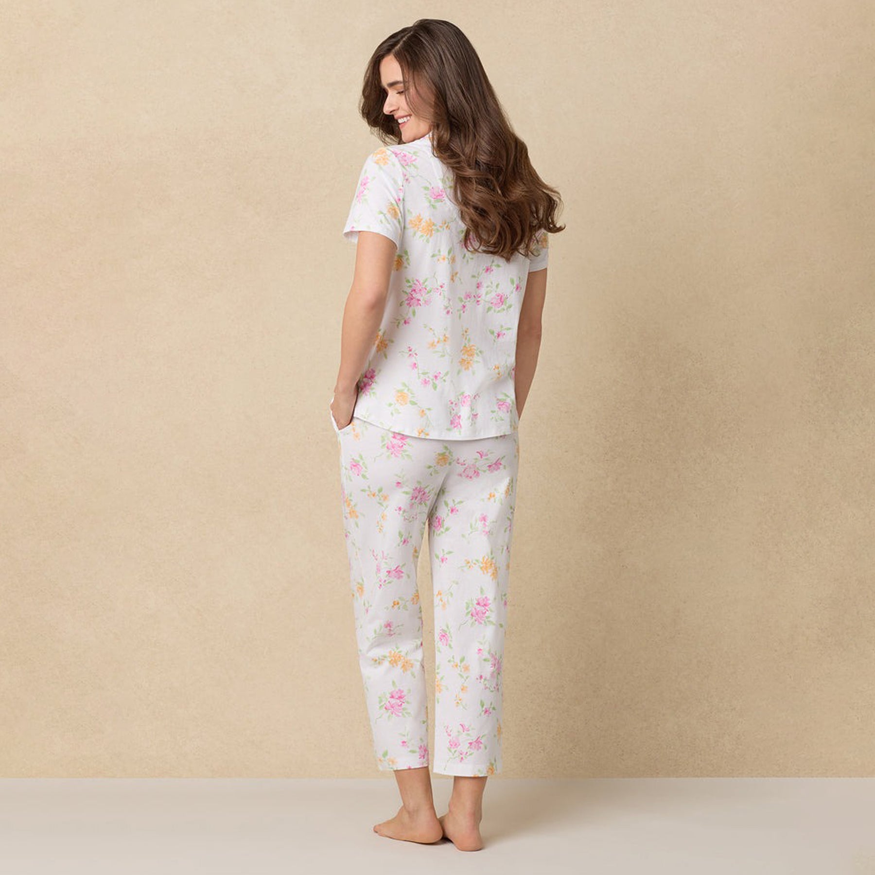 Back view of a woman wearing cropped floral pajama pants and a short-sleeve button-up top.