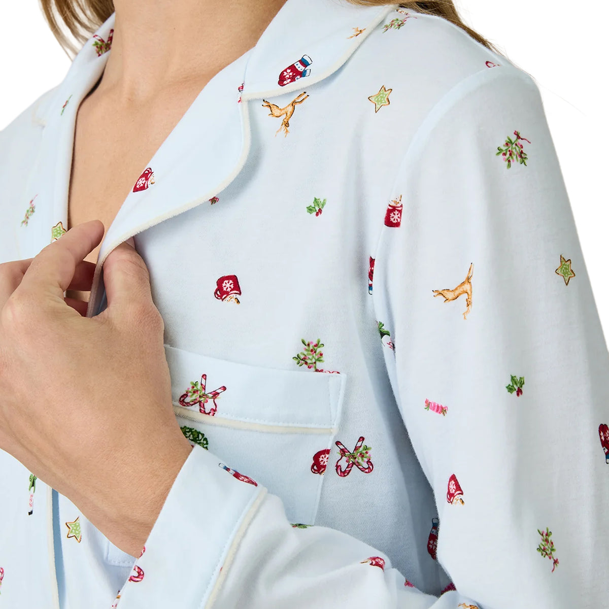 Close-up of Carole Hochman light blue holiday pajamas showing white piping along the notched collar and chest pocket, with festive prints of reindeer, stockings, candy canes, holly and stars.