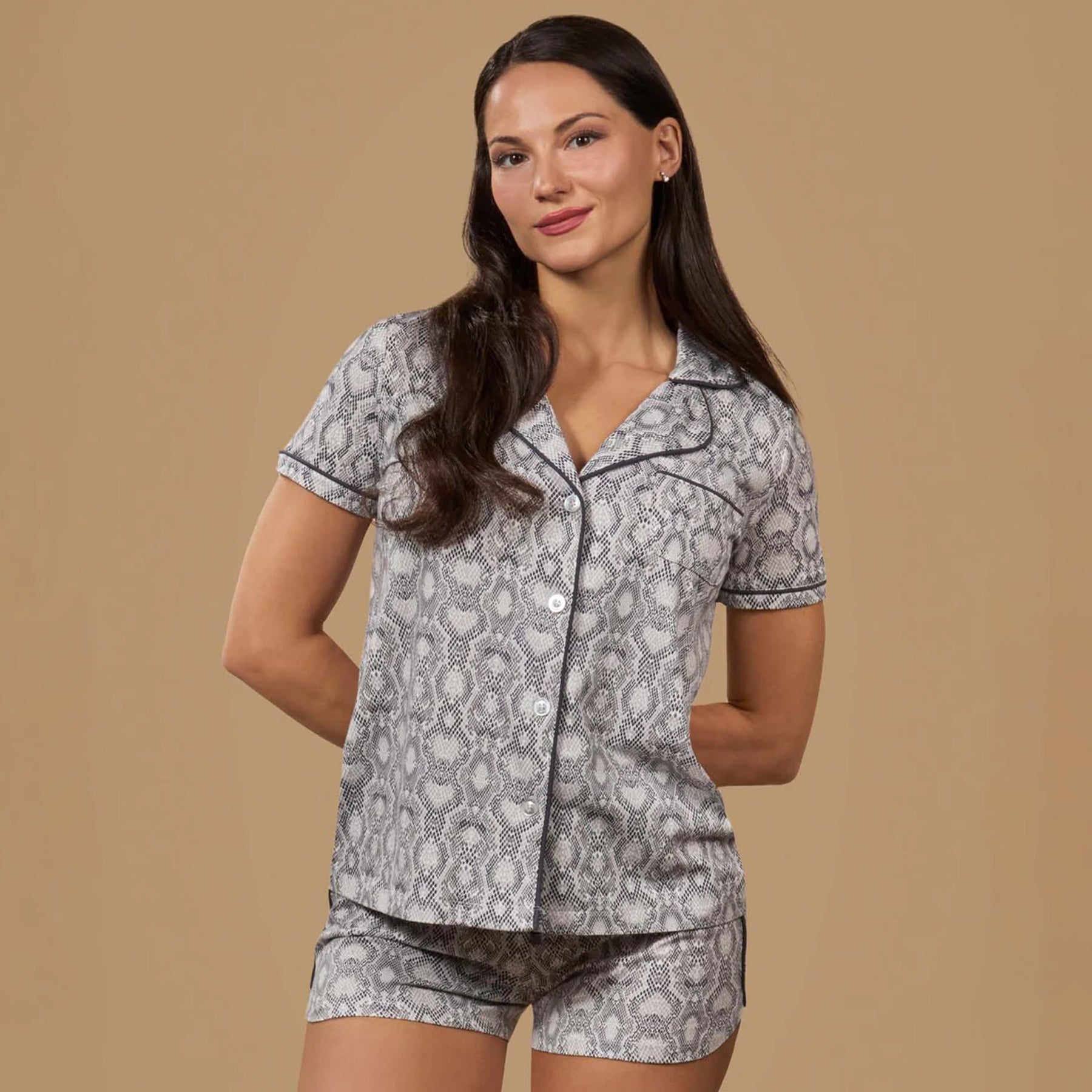 Model wearing grey snake print short sleeve pyjama set with button-up top and relaxed fit shorts on neutral background.
