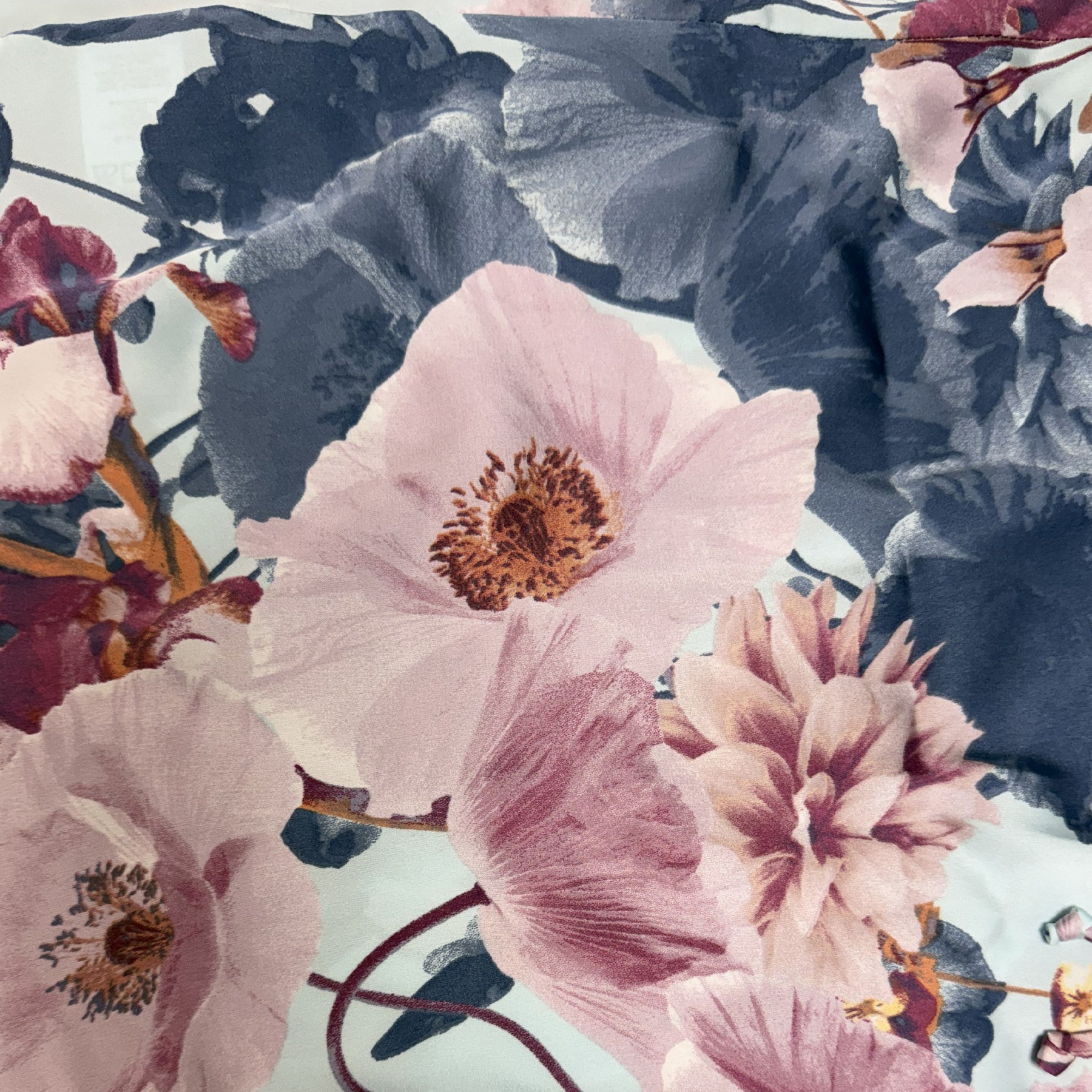 Close-up of light blue satin fabric with oversized blush pink florals and deep navy botanical print showing smooth, silky texture.