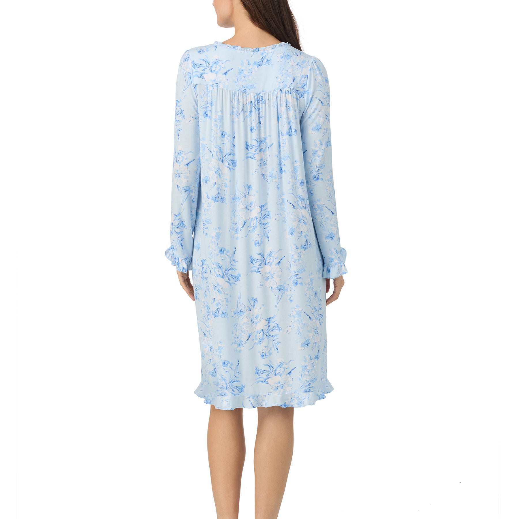 Back view of a woman wearing a light blue floral nightgown with long sleeves and ruffled hem.
