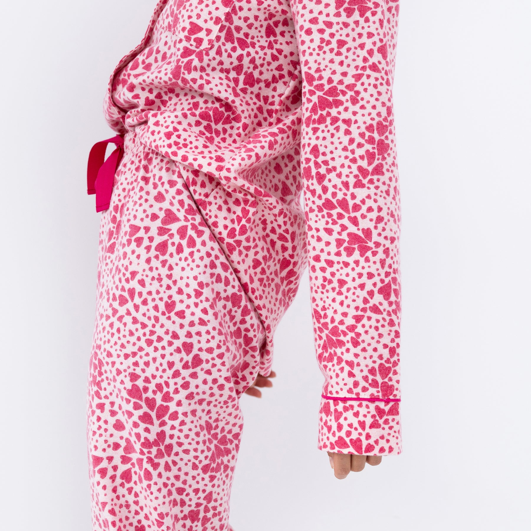 Close-up side detail of pink heart-print cotton pyjama sleeve and pants hem, showing fine piping trim.