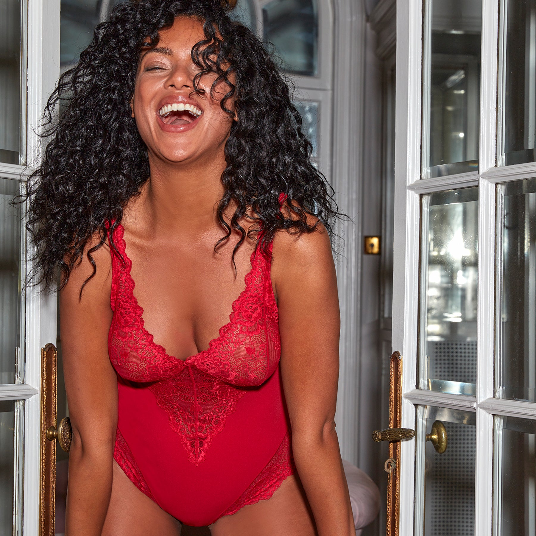 Janira Greta red lace bodysuit styled on model in an interior setting, highlighting elegant lace detailing and flattering fitted silhouette