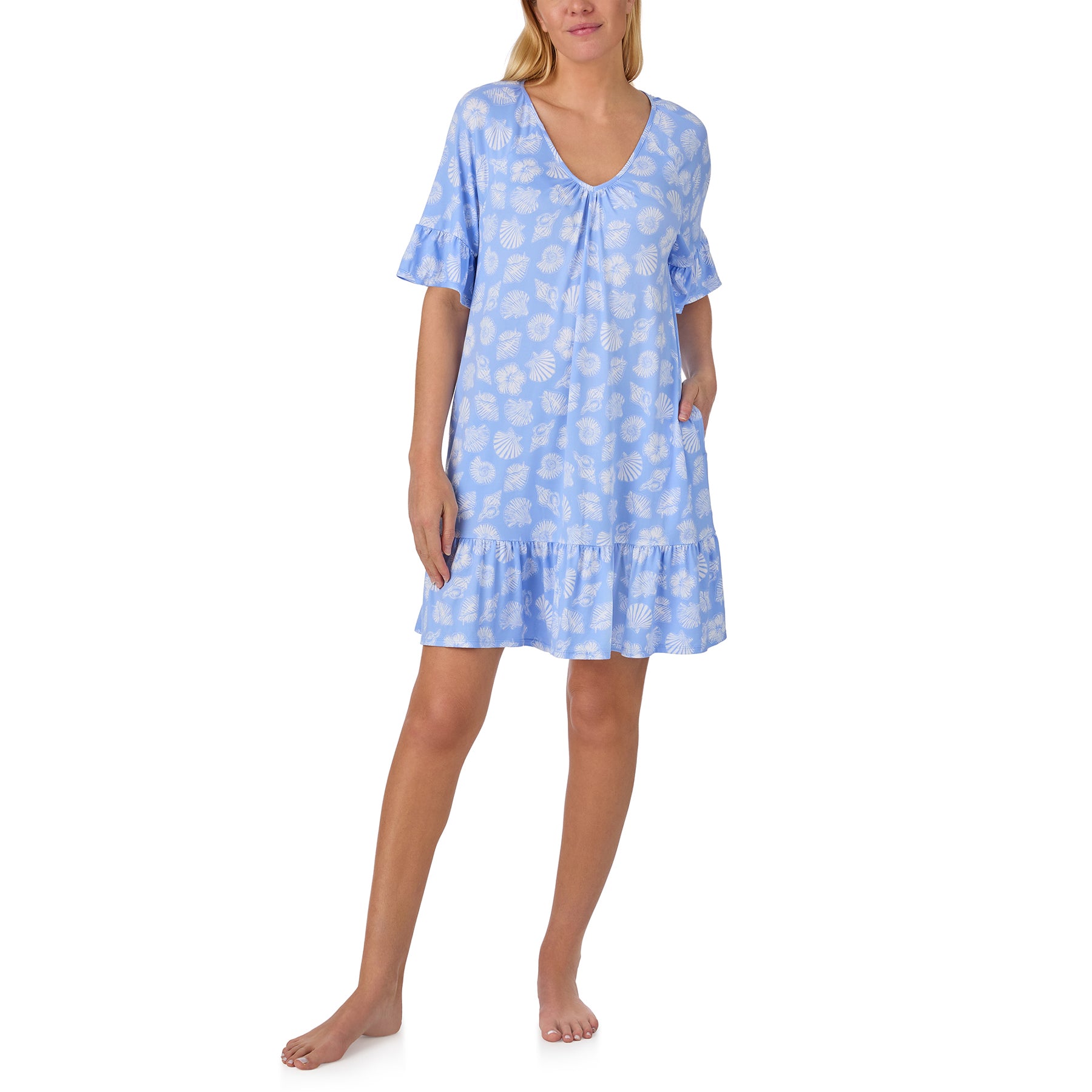 Woman wearing a light blue Ellen Tracy sleep shirt featuring a white seashell print, flutter sleeves, a soft V-neckline, side pockets, and a relaxed silhouette with a ruffled hem.