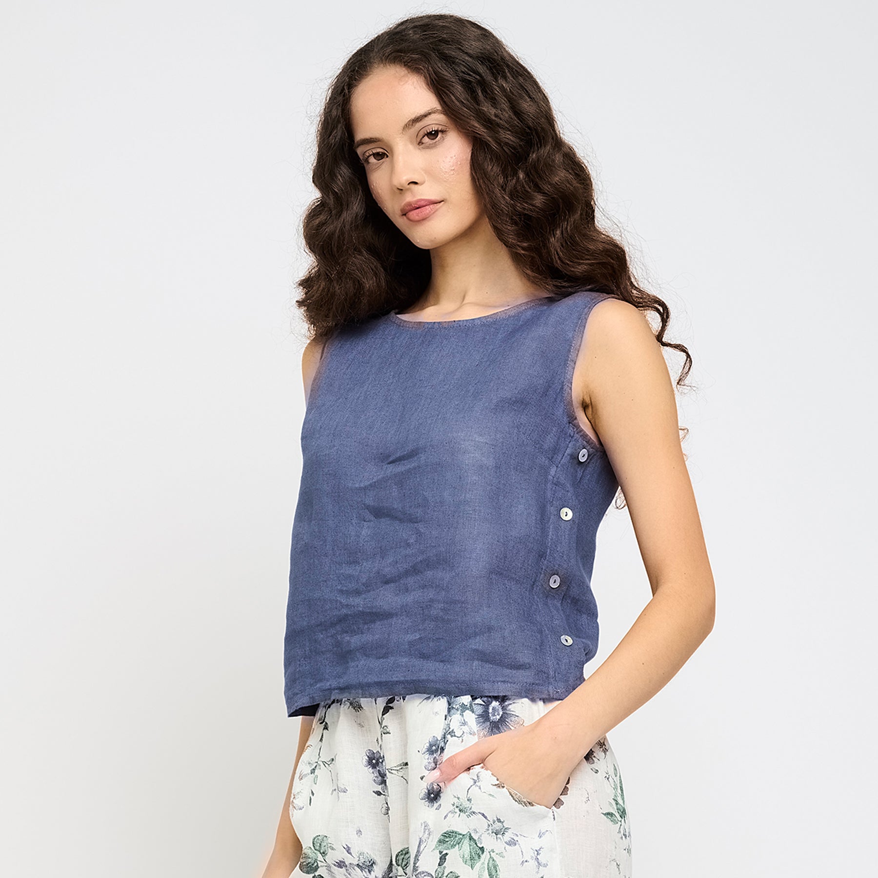 Woman wearing a sleeveless deep sea blue linen top featuring side button details - lightweight and breezy summer style.